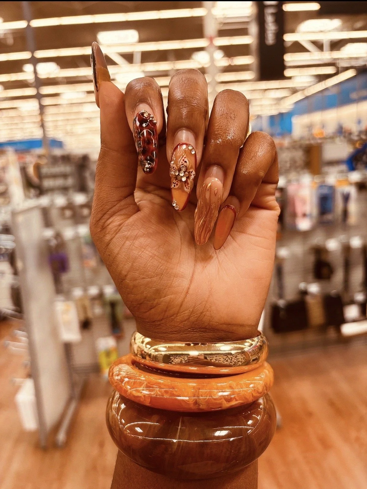 Kenya Brown In Walmart taking a Close-up hand photo with her colorful, decorative acrylic nails and several chunky bracelets that compliment her earthy and bold style.