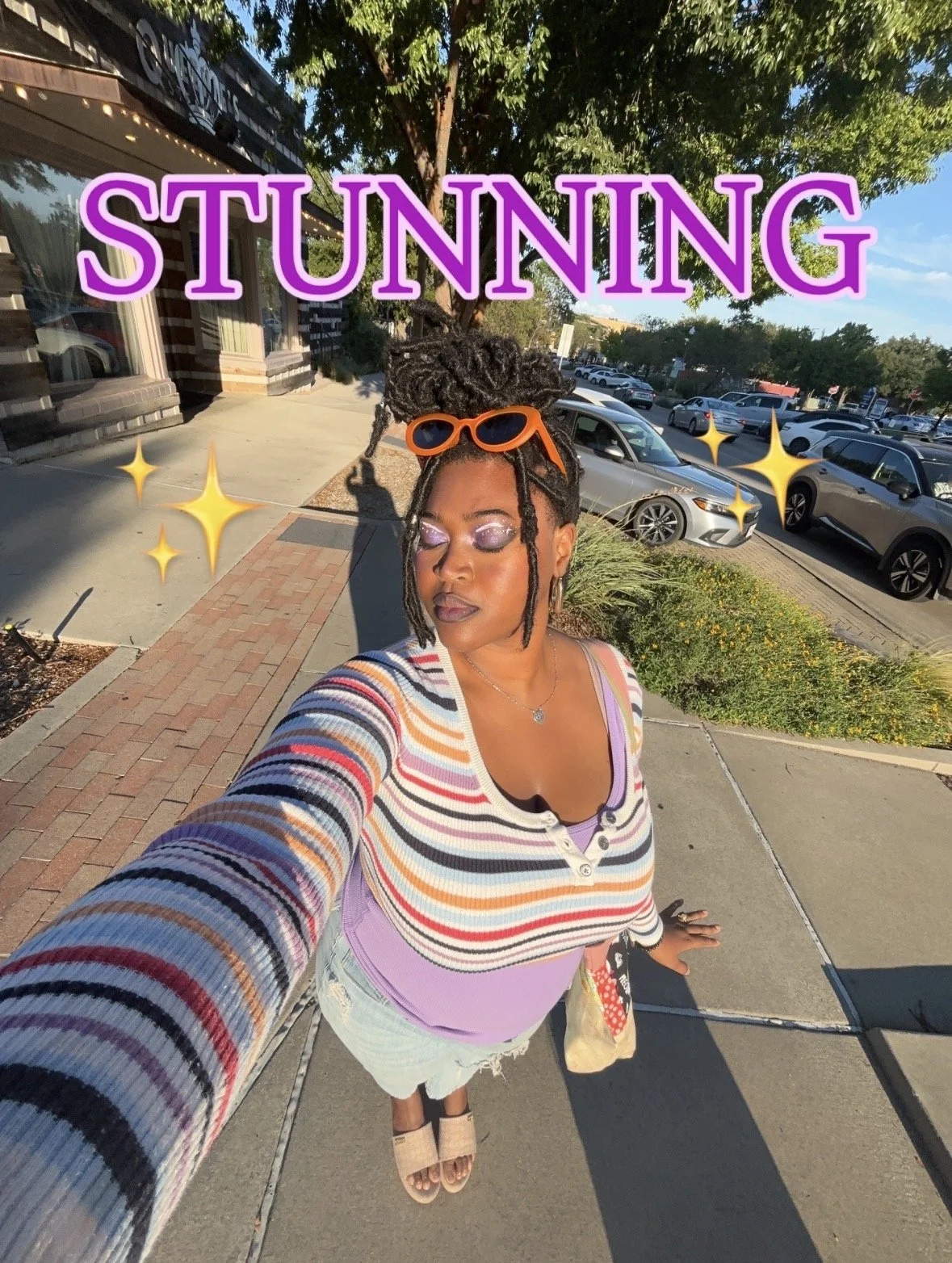 Kenya Brown taking a selfie in the heart of Denton Square before selling her one of a kind art. Dressed in a rainbow top, purple shirt and makeup and orange sunglasses.