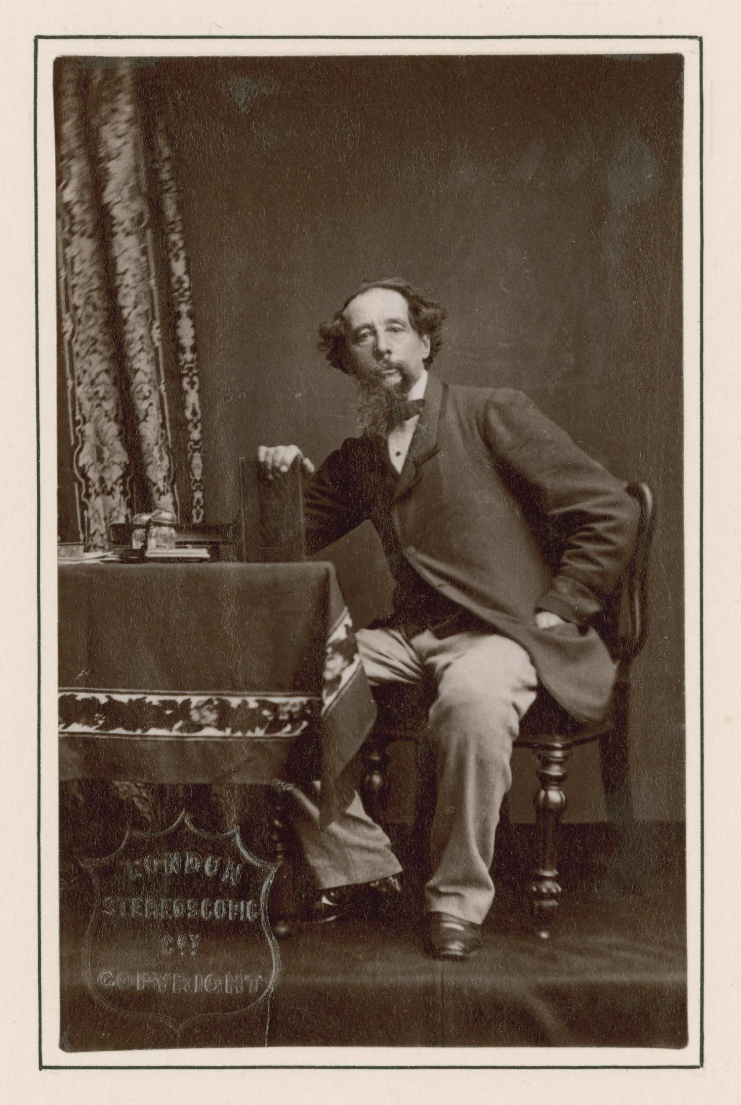 C. Natkins. [Photograph of Charles Dickens sitting at table with book], photograph, 1861.