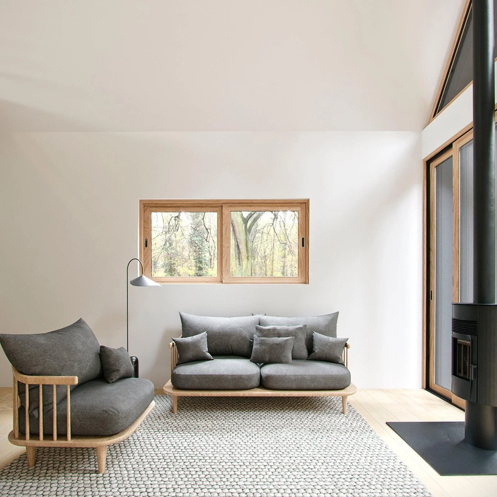 Living room with a gray sofa and matching armchair, a window showing trees outside, a floor lamp, a patterned rug, and a black stove.