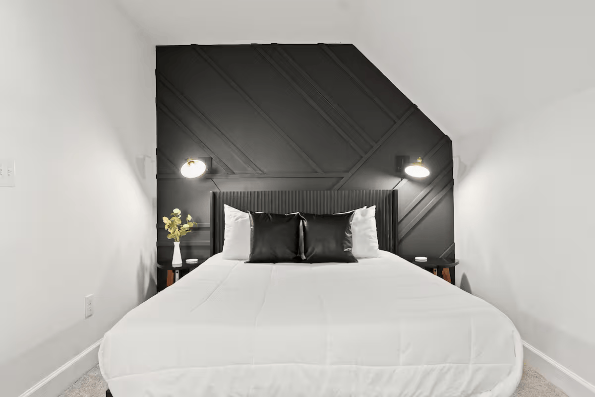 A neatly made bed with white bedding, black and white pillows, and a black headboard, flanked by black bedside tables with lamps in a modern bedroom.