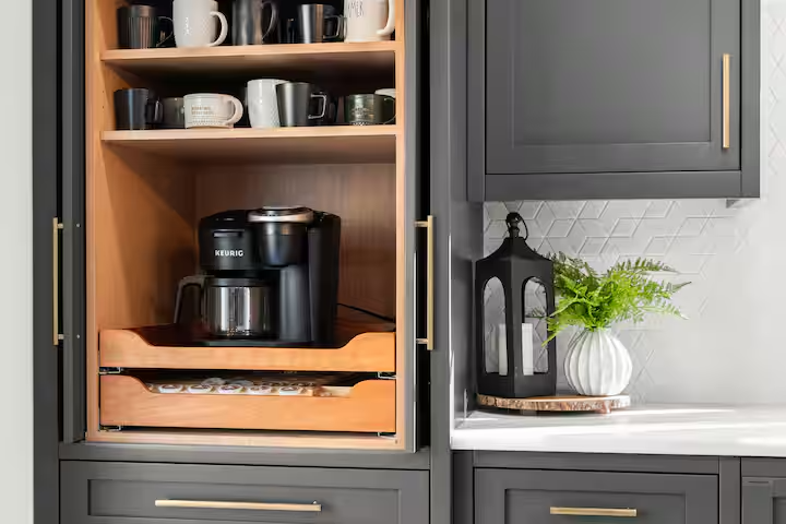 Kitchen cabinet with shelves holding mugs, a coffee maker, and a decorative lantern with a plant on the countertop.