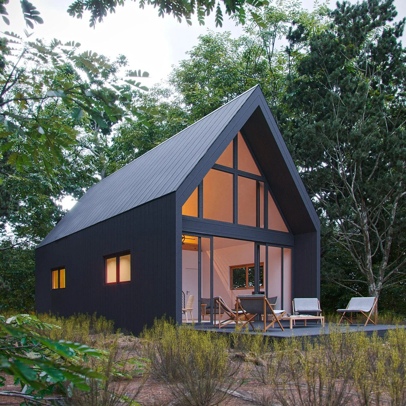 A modern black house with a steep gable roof and large glass windows, situated among trees and shrubs. The house has a porch with outdoor chairs and a table, illuminated from inside.