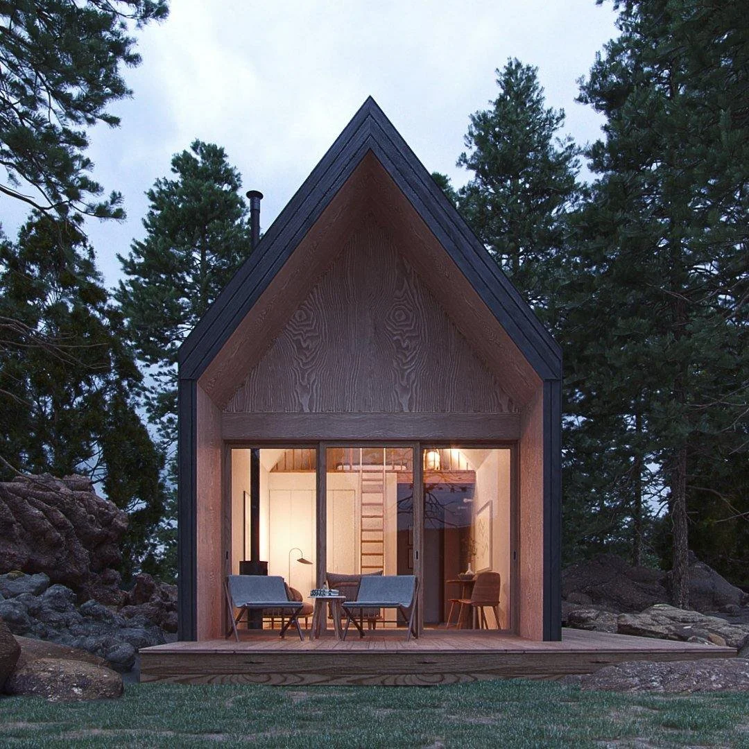 Modern A-frame cabin with wooden exterior, large glass sliding doors, and a small porch, surrounded by trees and rocks at dusk.