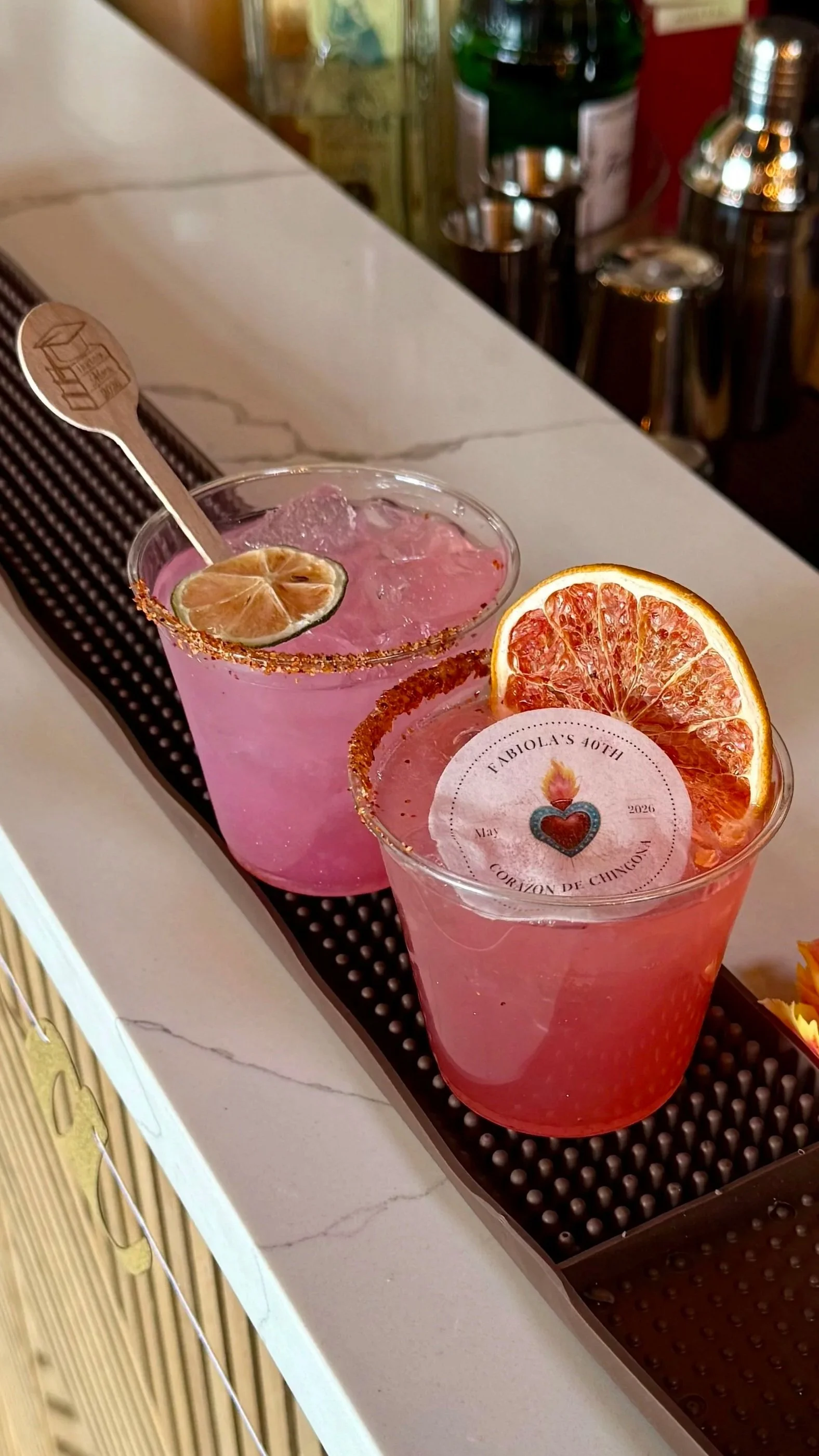 Two pink cocktails with dried citrus slices and salted rims on a bar counter.