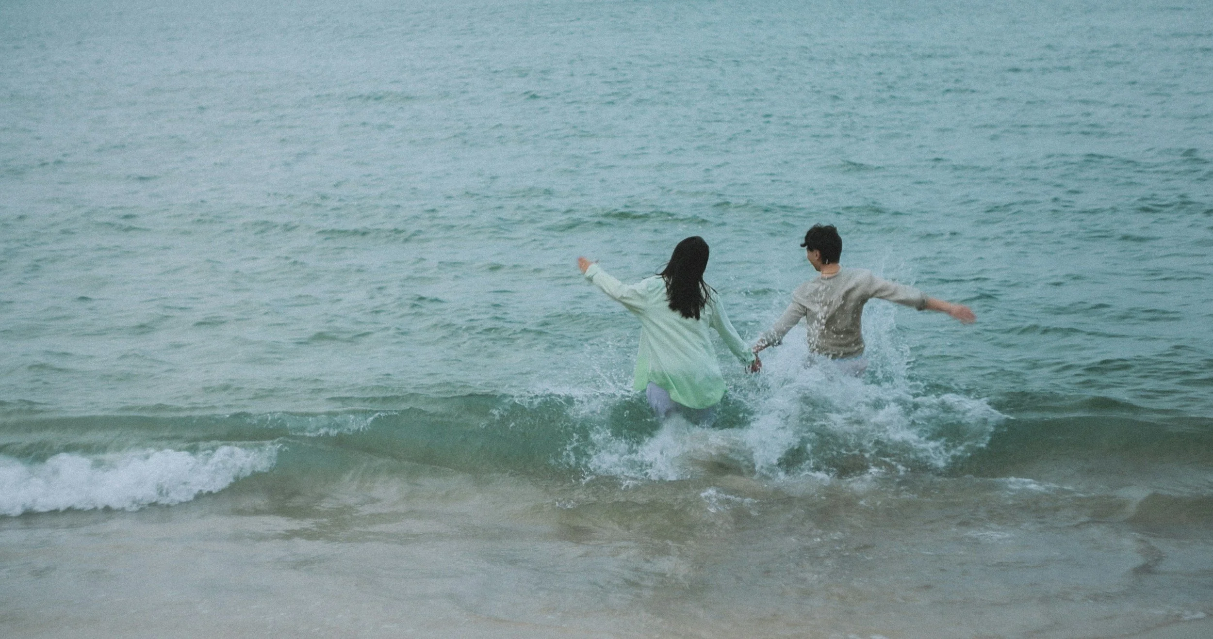 Couple holding hands and running into the ocean waves at the beach.