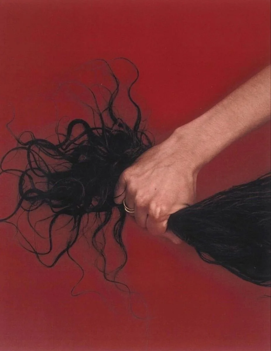 A person with a light skin tone is holding a bunch of long black hair with their hand on a red surface.
