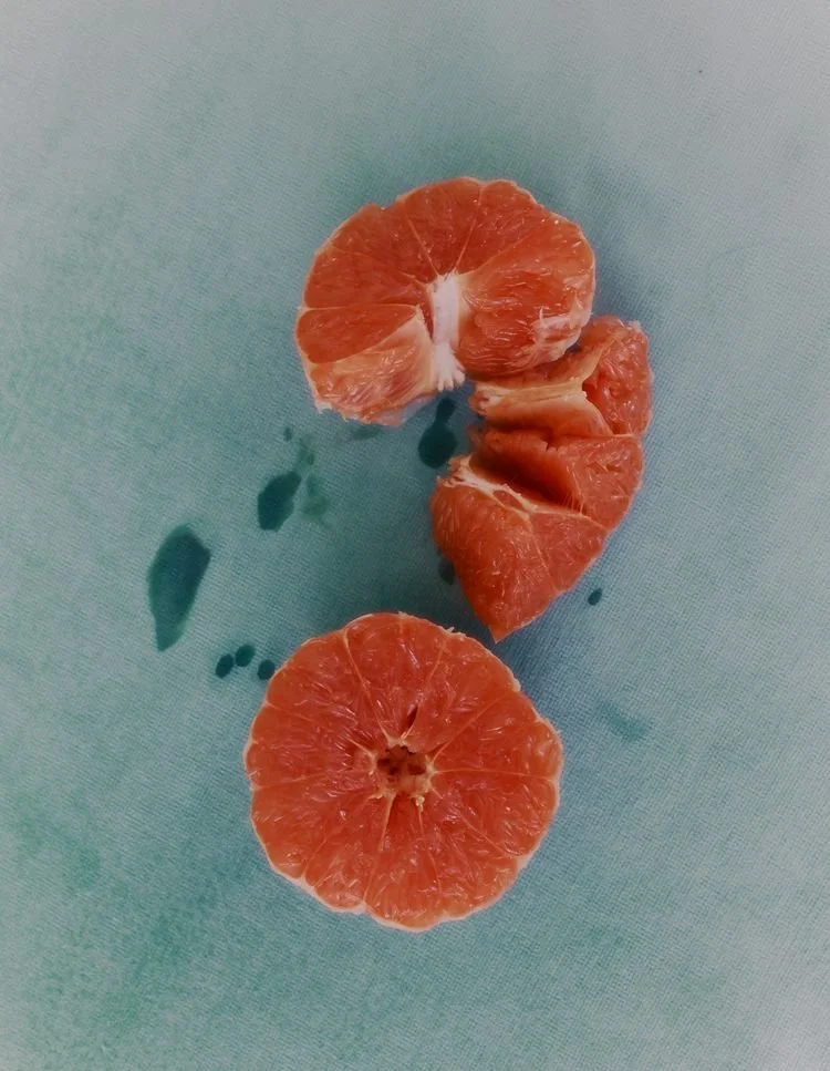 Multiple peeled tangerine segments on a light blue surface with juice droplets.