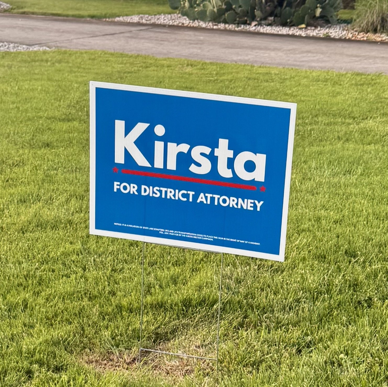 A political campaign sign on a lawn supporting Kirsta for District Attorney.