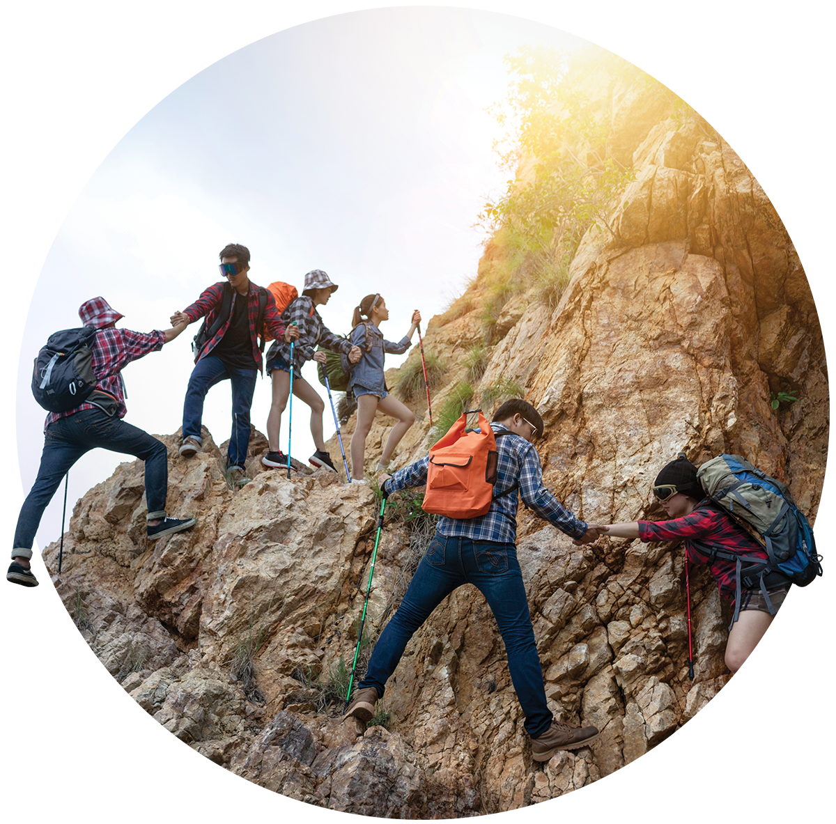 Group of young hikers climbing a rocky mountain slope, assisting each other, with one person helping another up the rocks, carrying backpacks and using hiking poles.