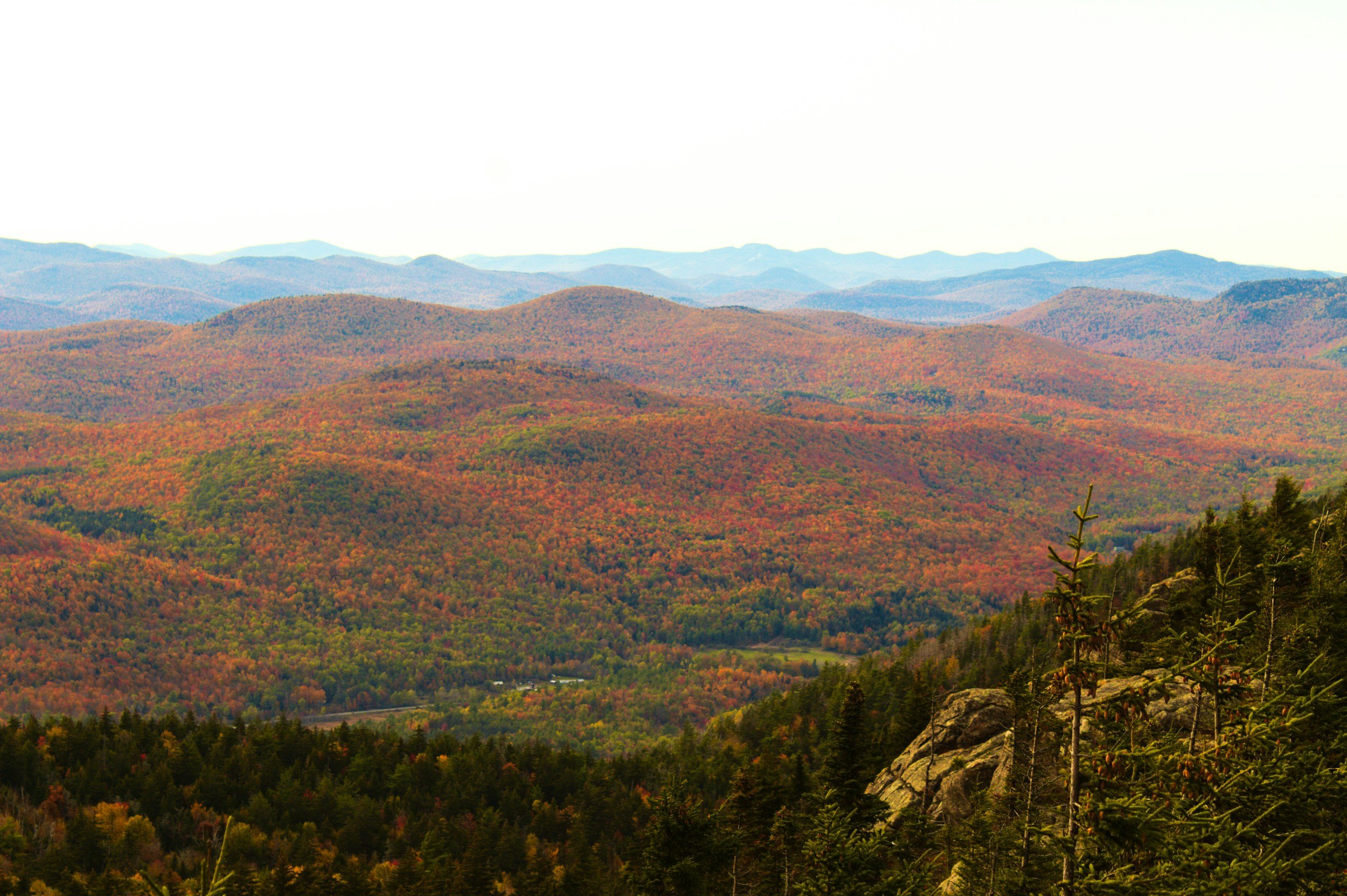 Scenic view of colorful autumn mountains with trees in various shades of red, orange, yellow, and green, and a rocky outcrop in the foreground.