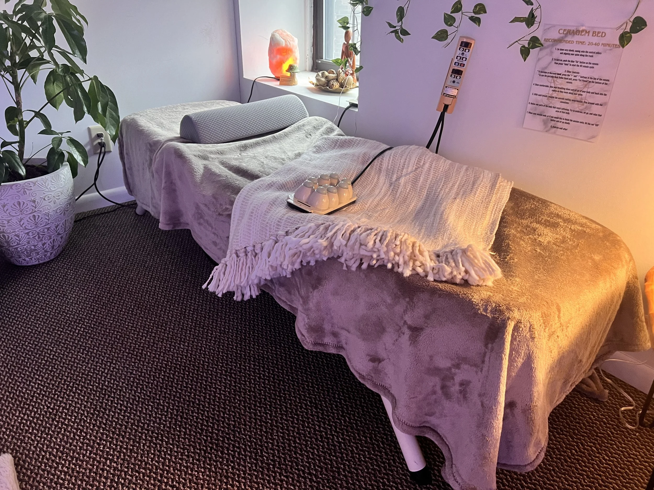 Bed with a gray pillow, a potted plant, a window with decorative items on the sill, including a salt lamp