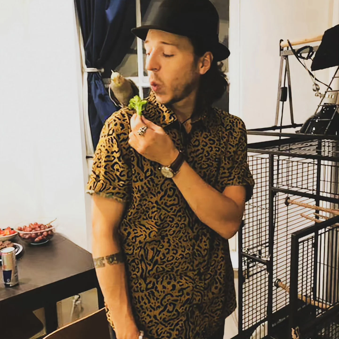 A man in a colorful shirt and black hat with a bird perched on his shoulder.
