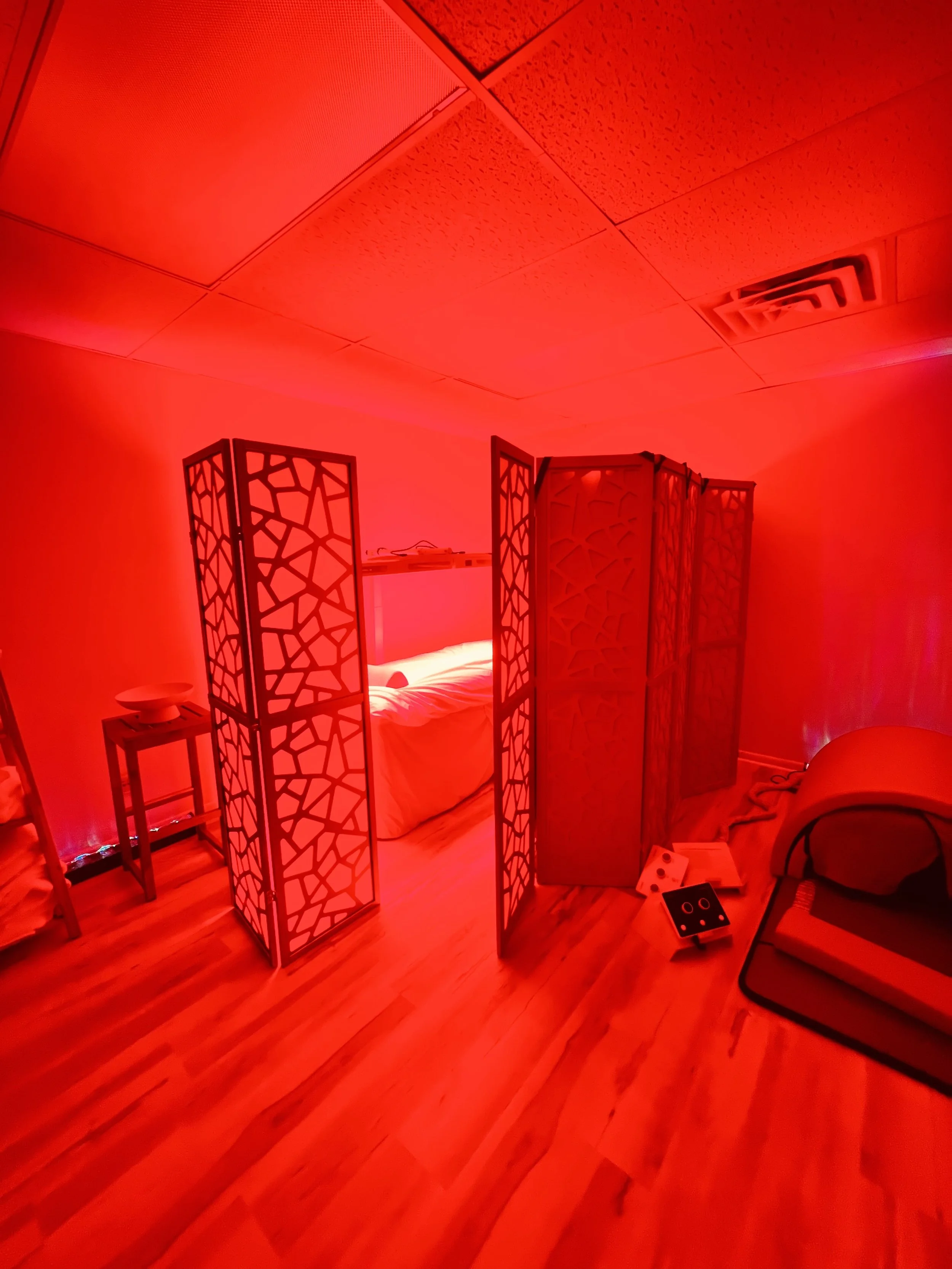 Room illuminated with red light showing a bed behind a folding decorative room divider.