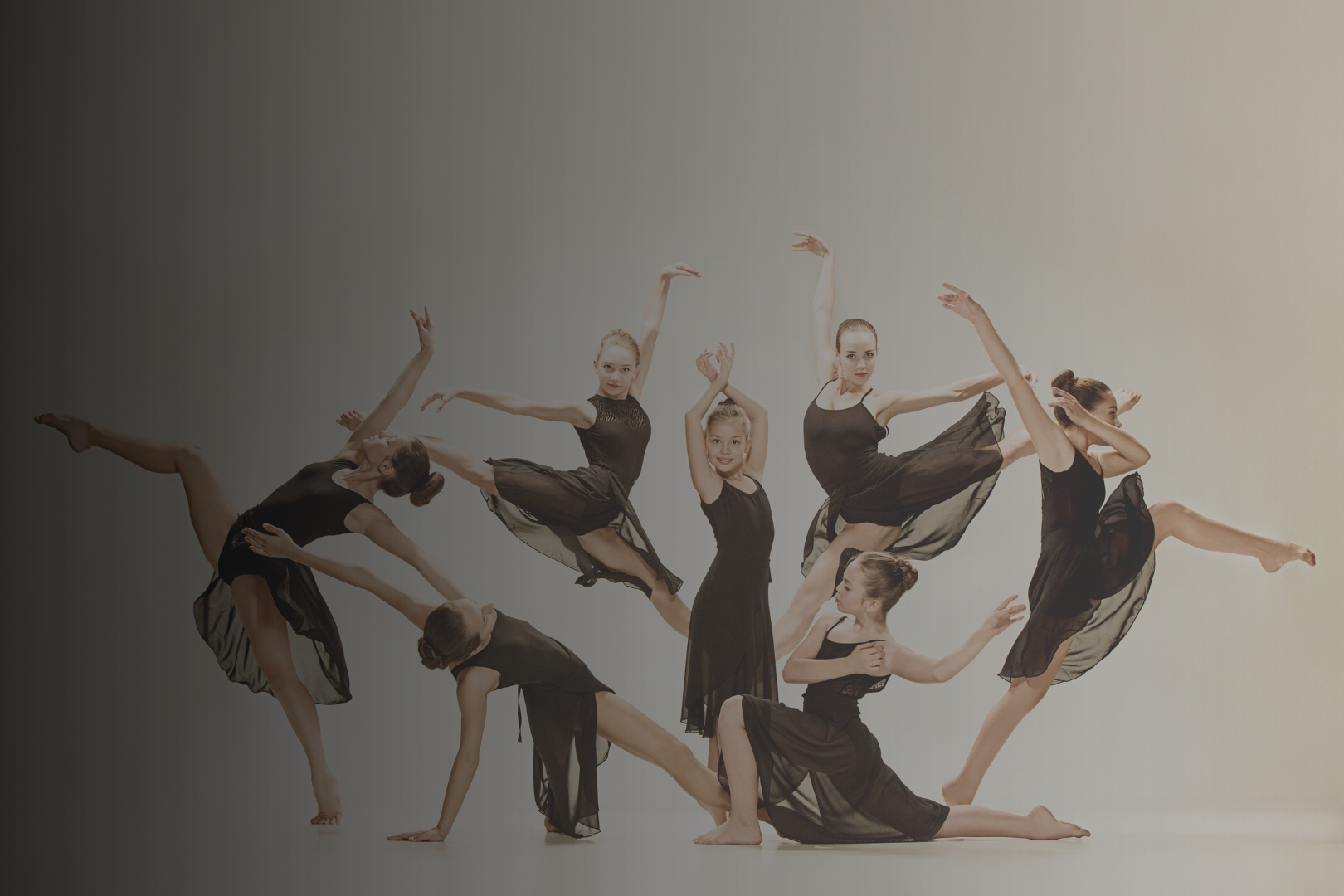 Group of young female ballet dancers in black costumes performing intricate poses against a light background.