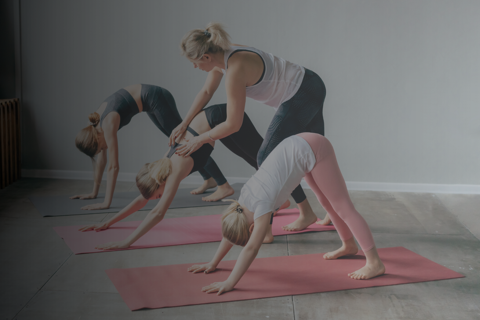 Group of women and girl practicing yoga in downward dog pose on mats in a room.