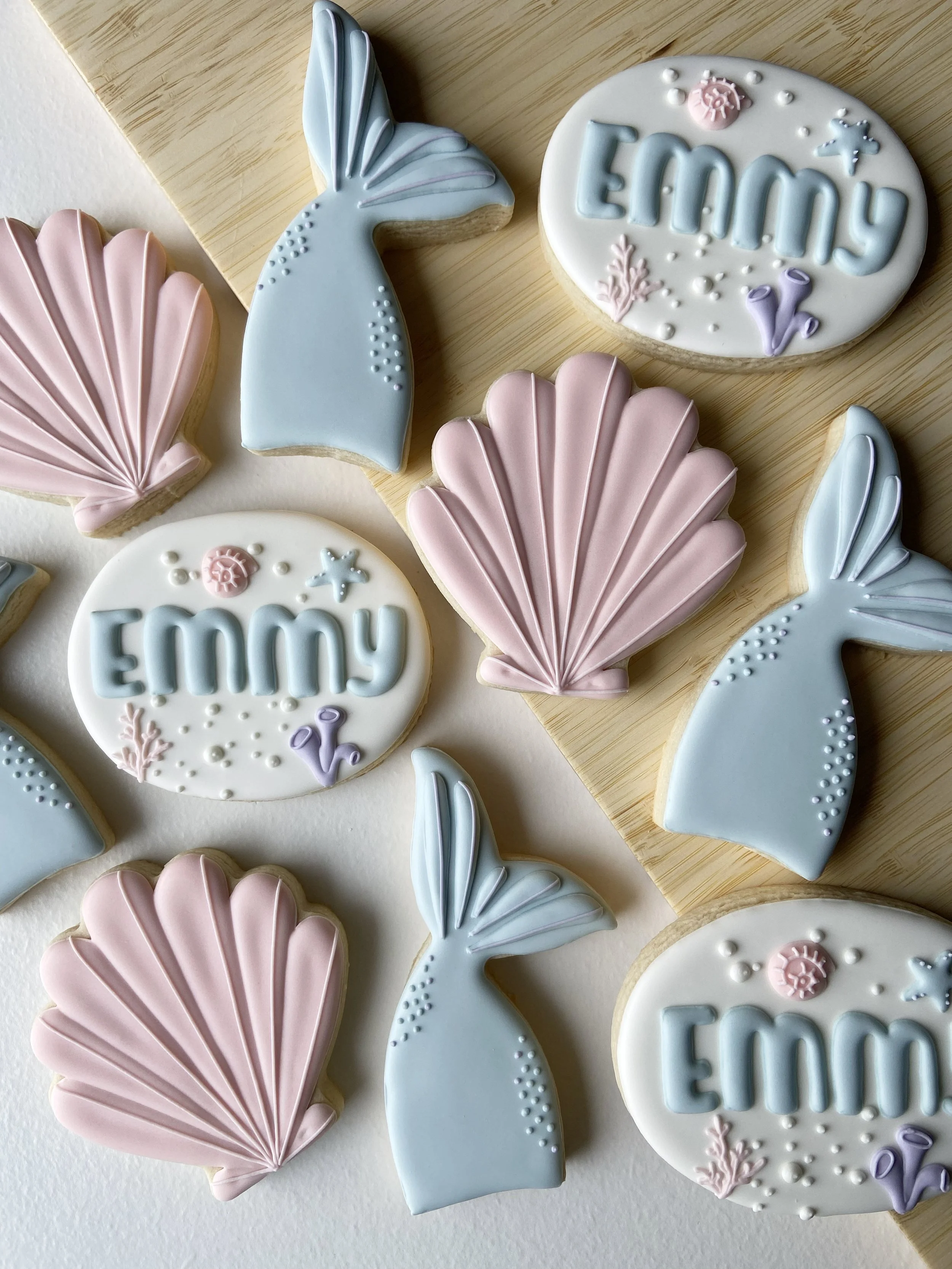 Decorative cookies shaped like seashells, bunnies, and oval cookies with the name "Emmy" and seashell and starfish designs.