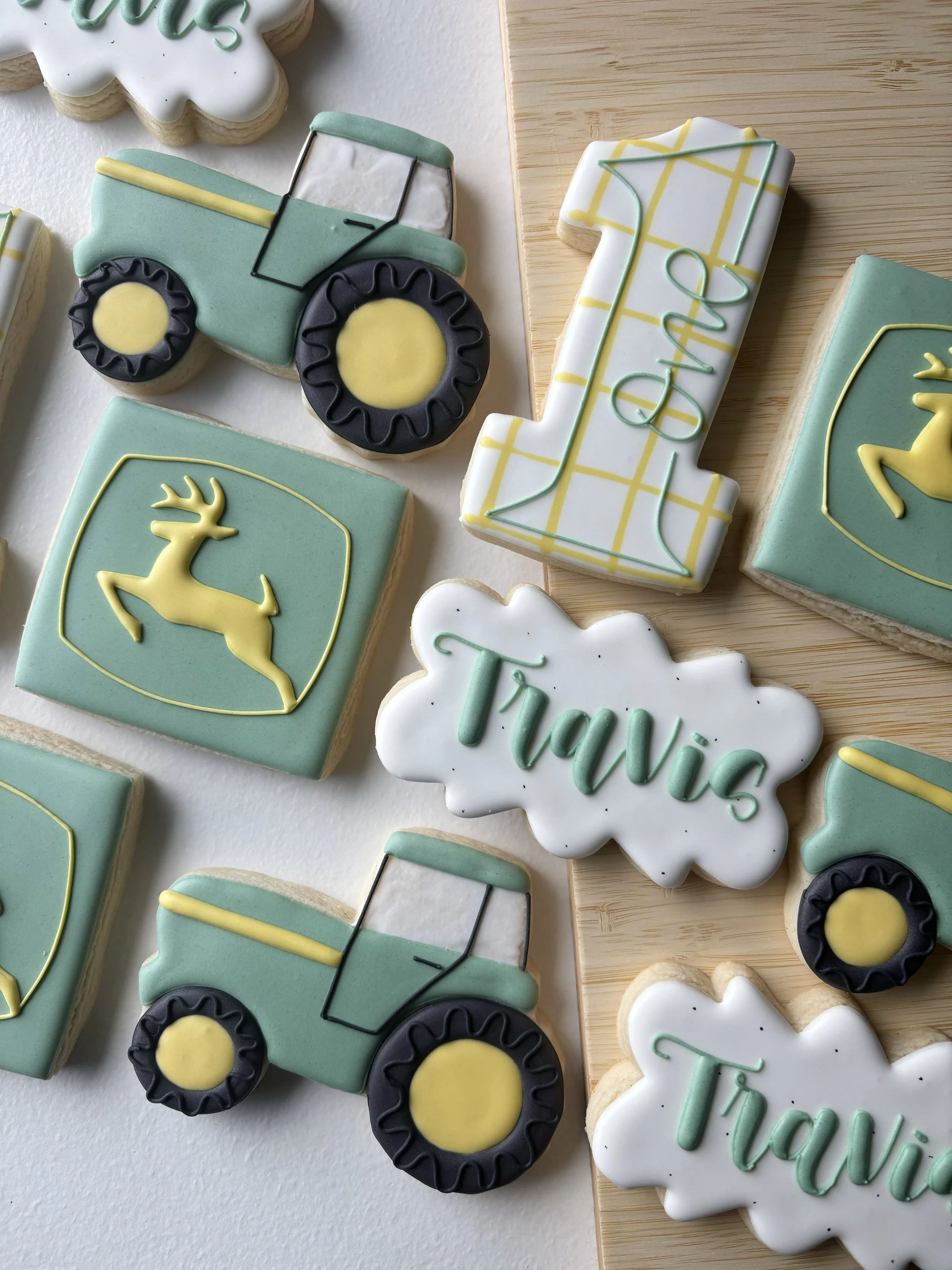Decorated cookies with a tractor, a deer, and the names 'Travis' and 'Madi' in pastel colors for a farm-themed celebration.