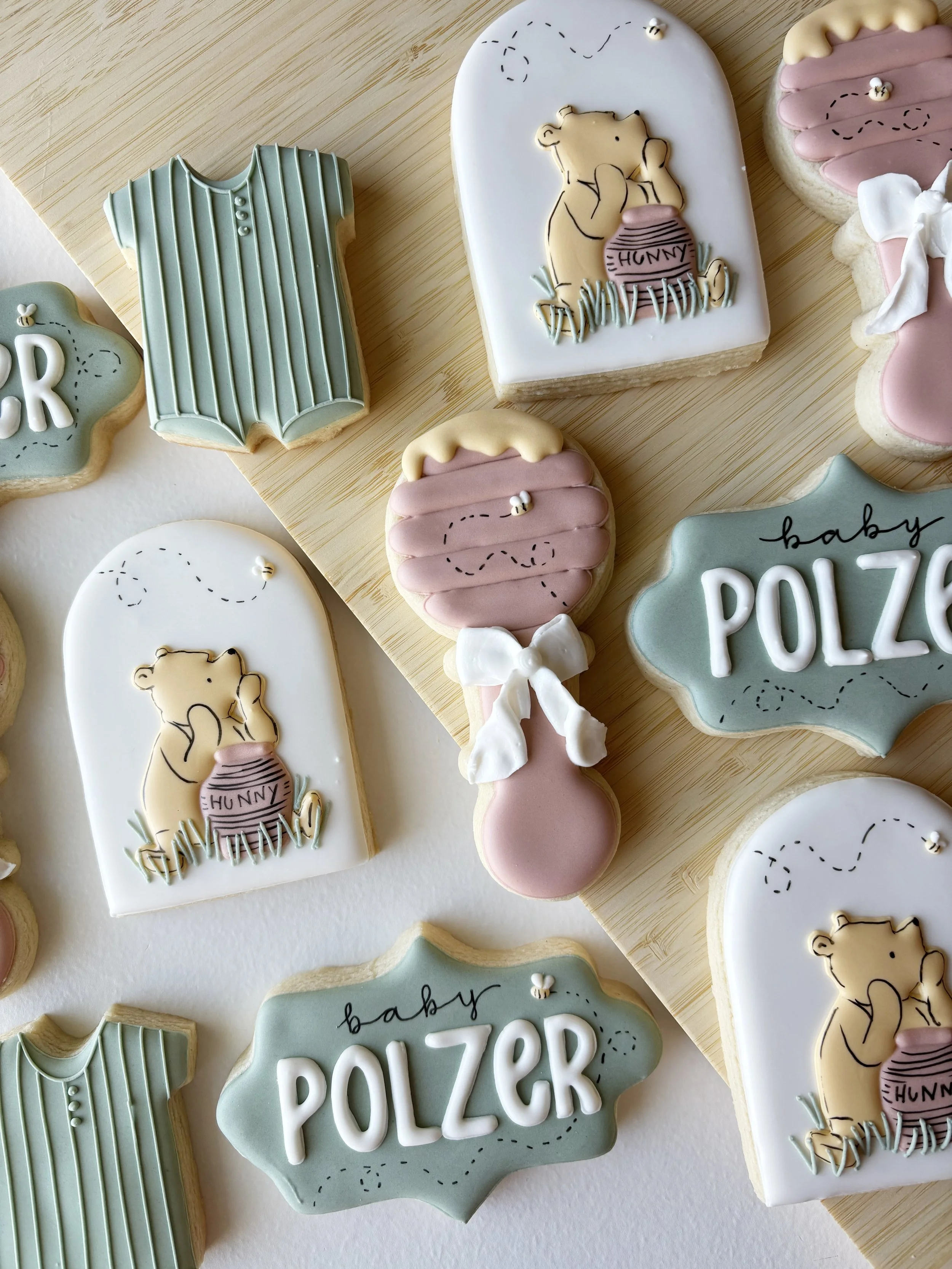 Decorative cookies with baby-themed designs and pastel colors, including a bear holding a jar labeled 'HUNNY,' a onesie, a balloon, and a sign that says 'baby POLZER'.