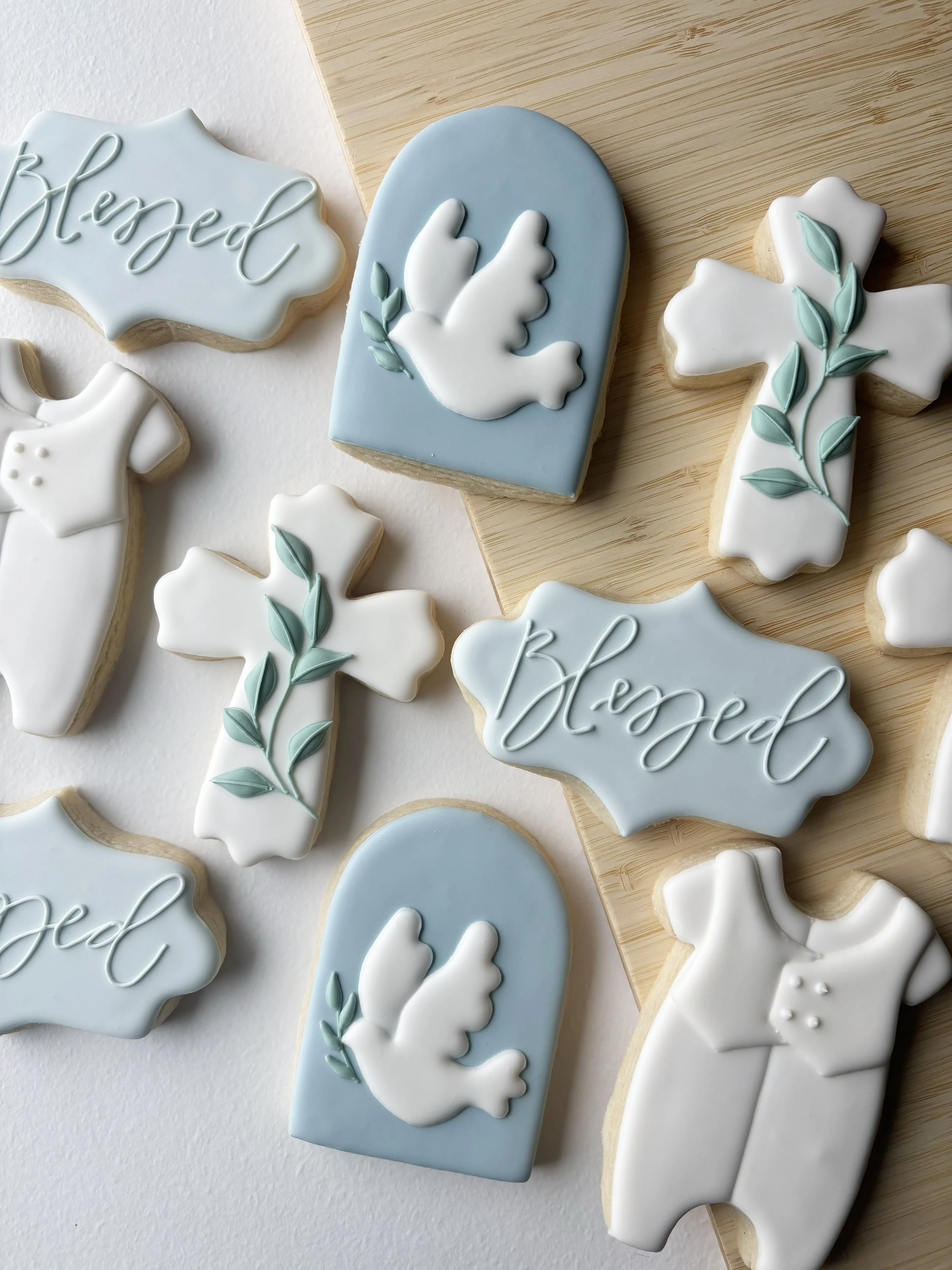 Cookies decorated with religious and spiritual symbols, including crosses, a dove, and the word "blessed" in elegant script.