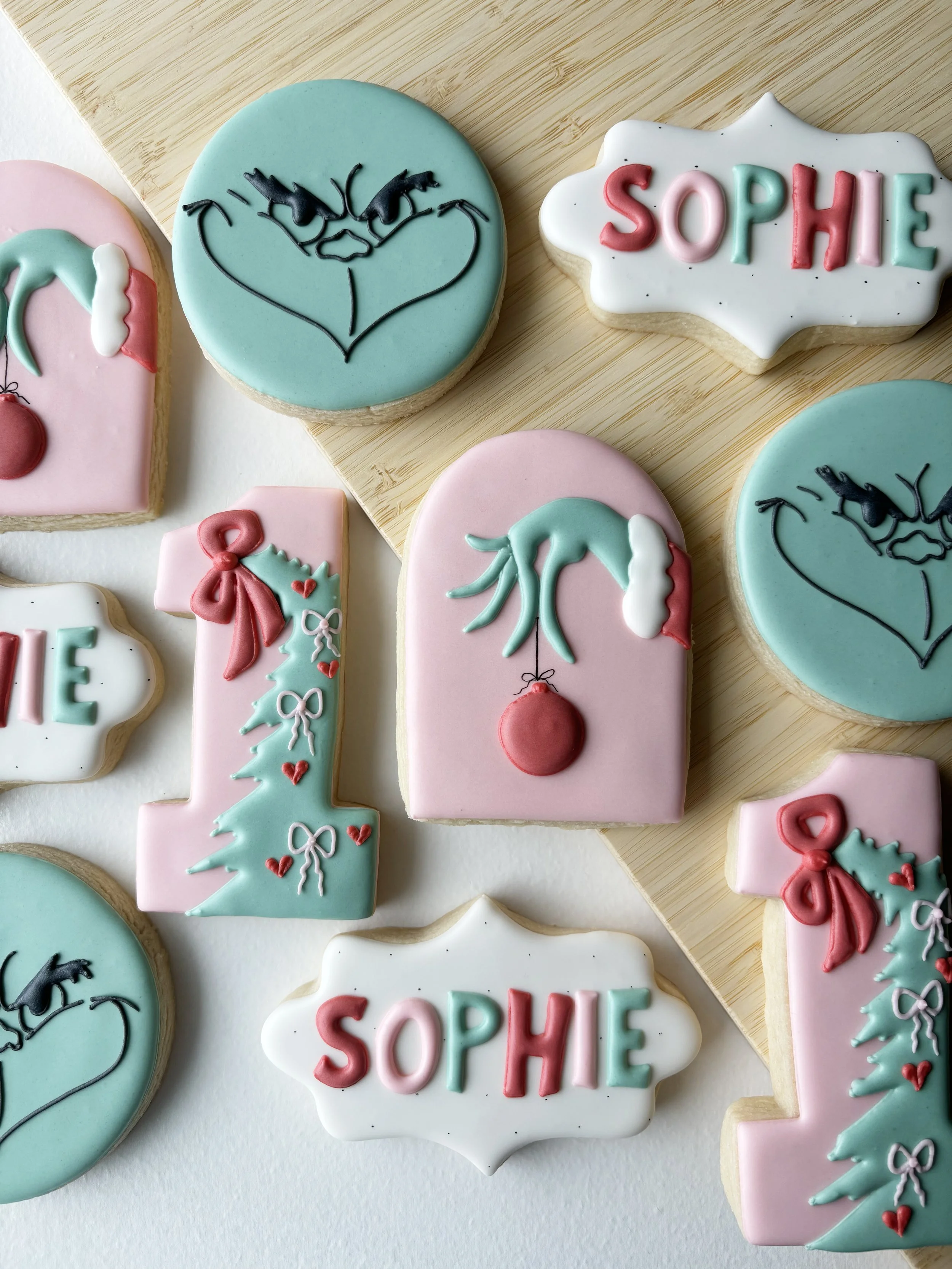 Christmas-themed cookies decorated with pastel colors, featuring a tree with a bow, a Christmas ornament, and the name 'Sophie'.