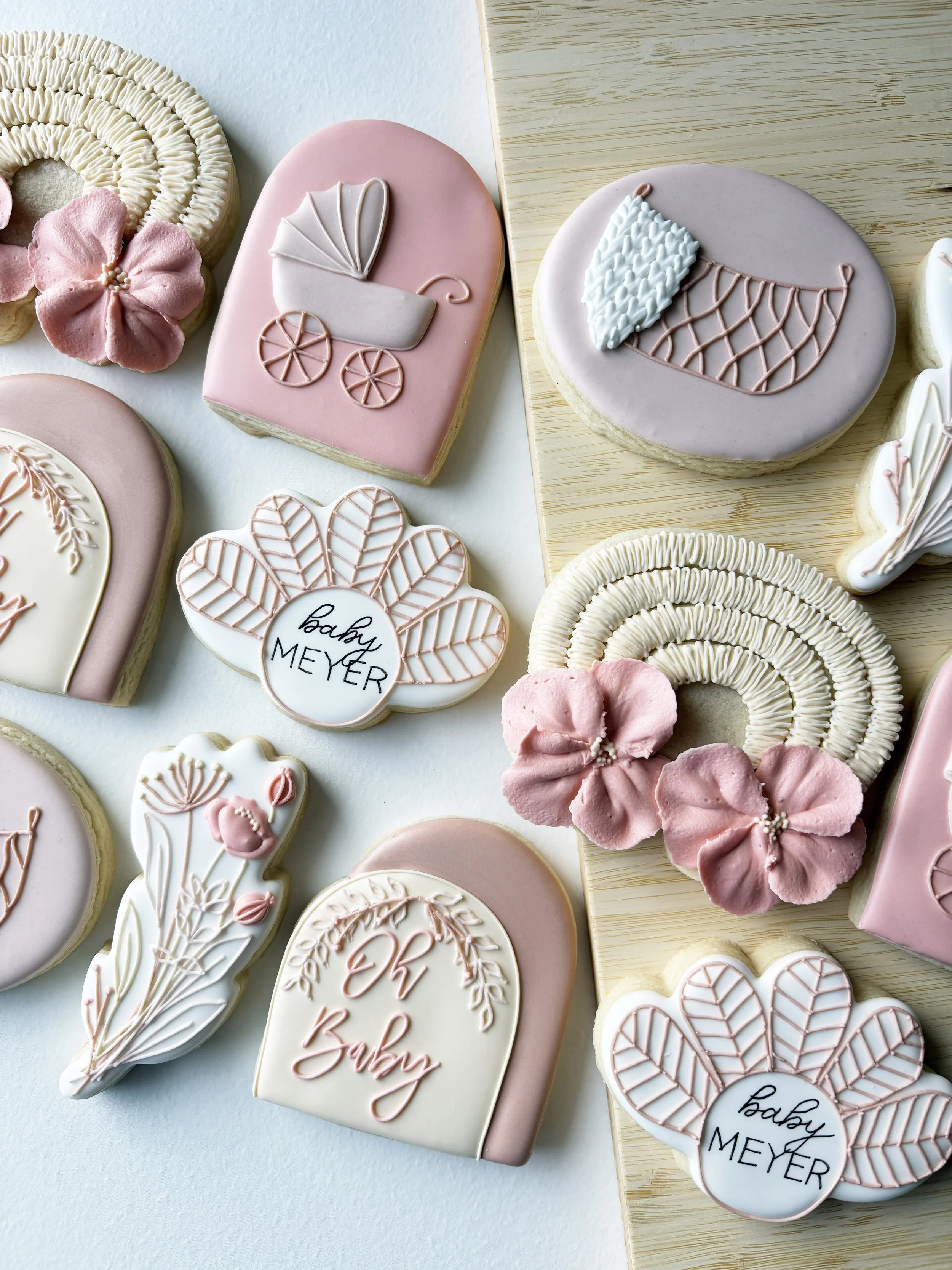 Decorated cookies for a baby celebration with pastel pink, white, and beige colors featuring baby carriages, flowers, and the text 'oh Baby' and 'baby MEYER'.