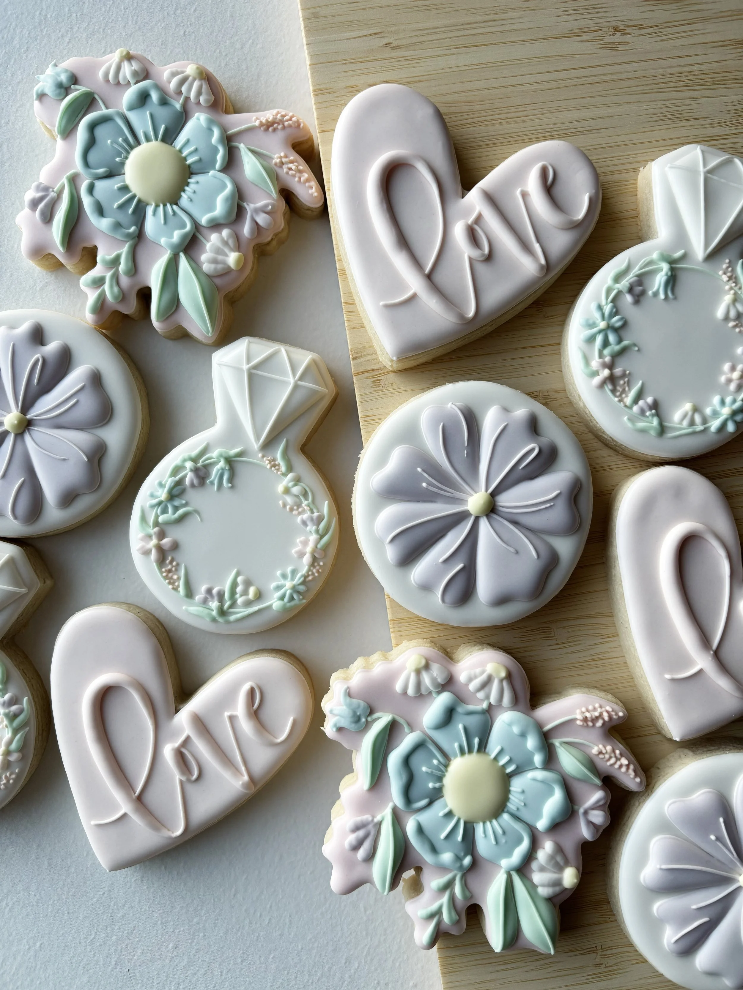 Cookies decorated with pastel-colored icing, some with flowers, hearts, and the word 'love' written in icing.