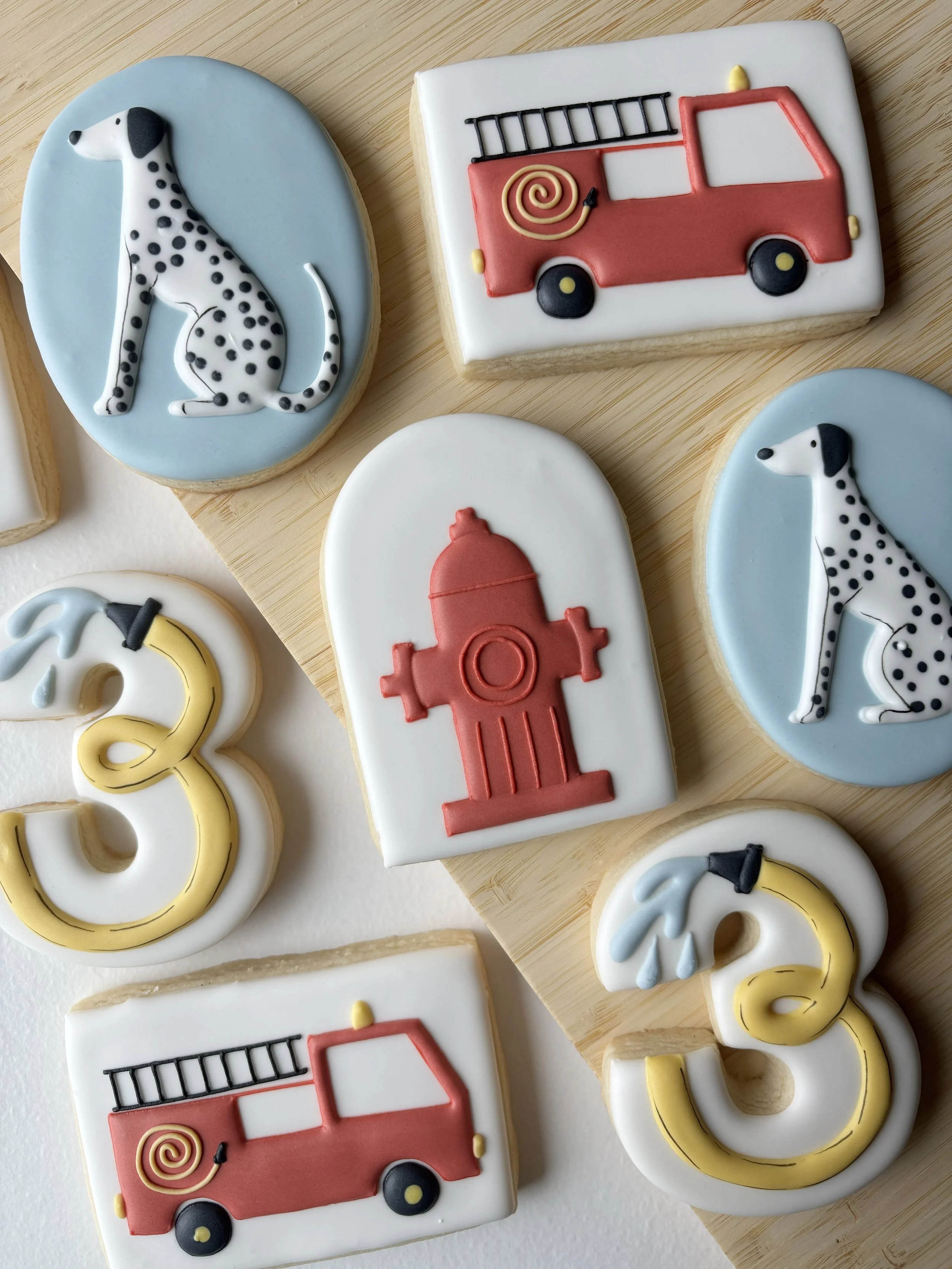 Decorative cookies featuring a Dalmatian dog, a fire truck, a fire hydrant, and a number three with blue water drops.