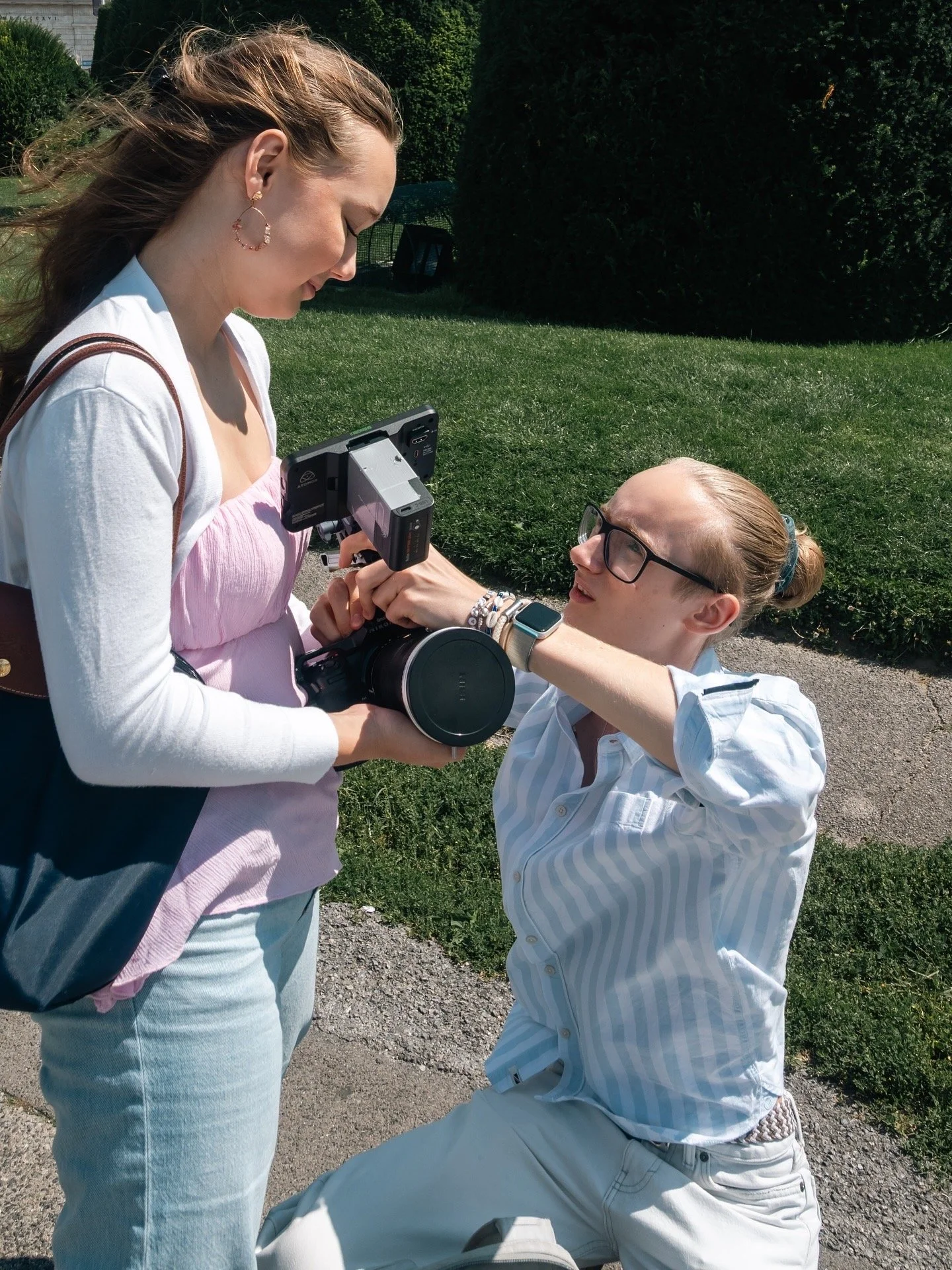 Zwei Frauen im Freien, eine sitzend und die andere stehend, beim Austausch eines Fotoapparats.