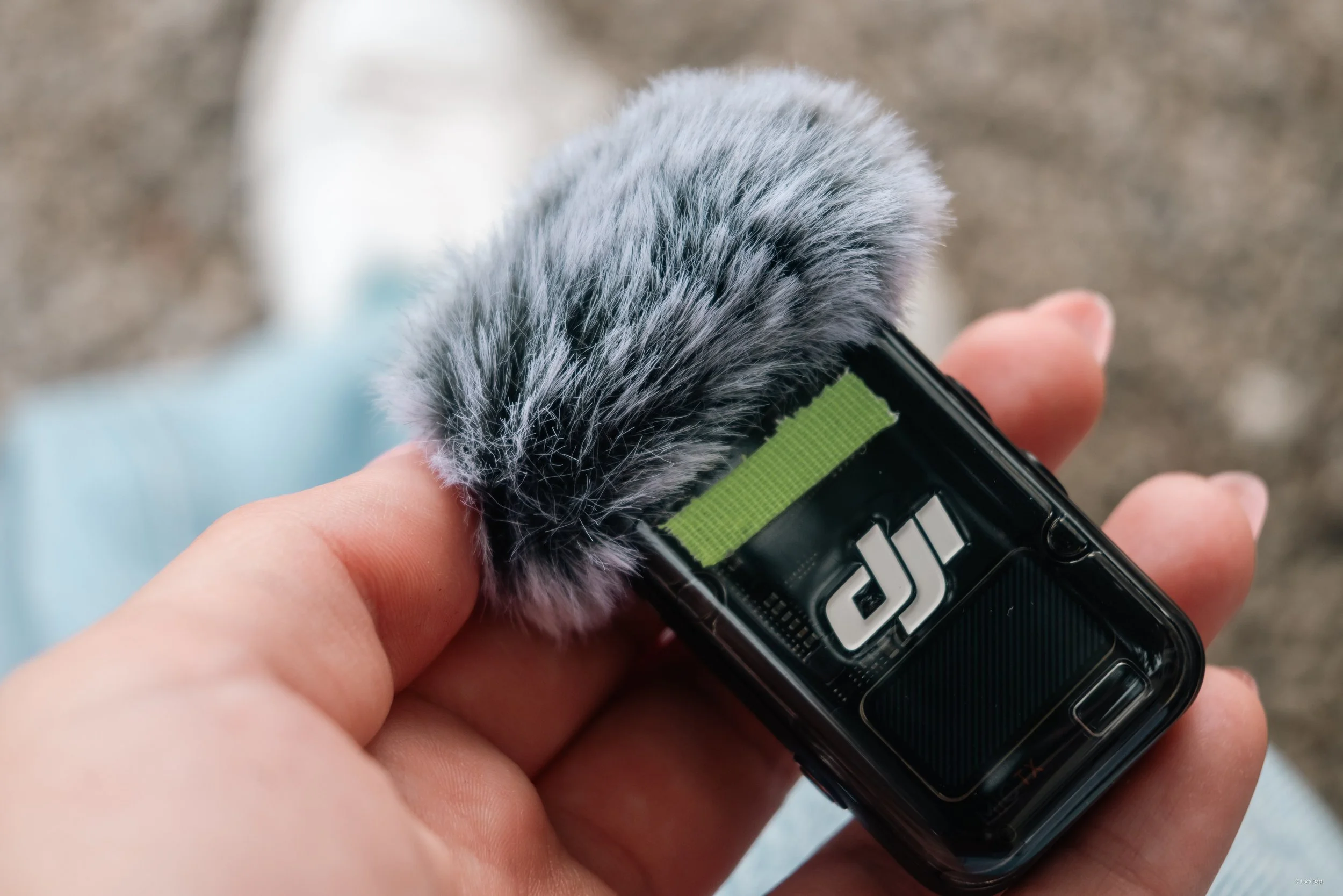 Nahaufnahme einer Hand hält einen schwarzen digitalen Tacho mit Fellüberzug an der Oberseite. Der Hintergrund ist unscharf und zeigt eine Außenszene.