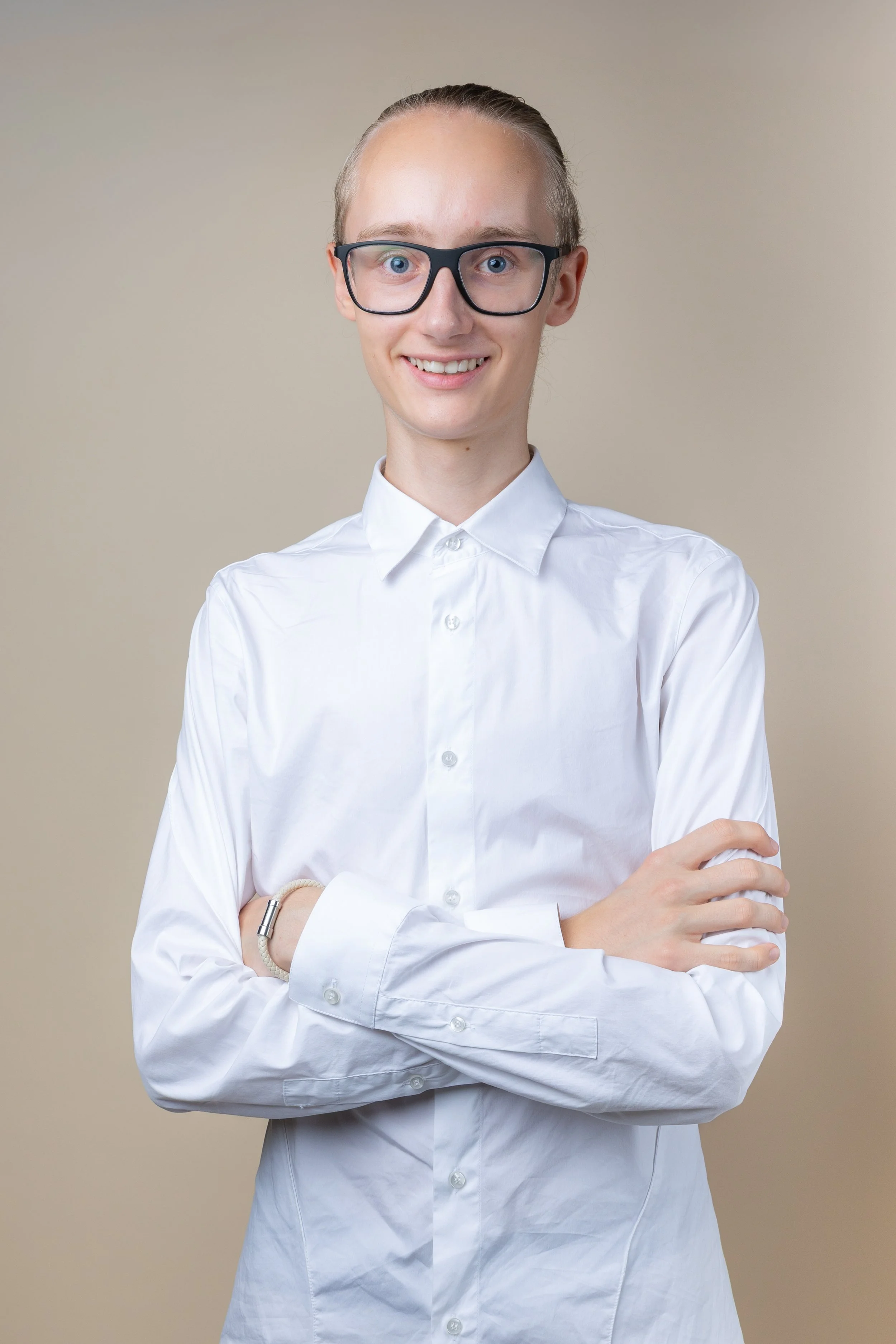 Porträt einer jungen Frau mit Brille, in weißen Hemd, lächelnd, stehen vor neutralem Hintergrund.