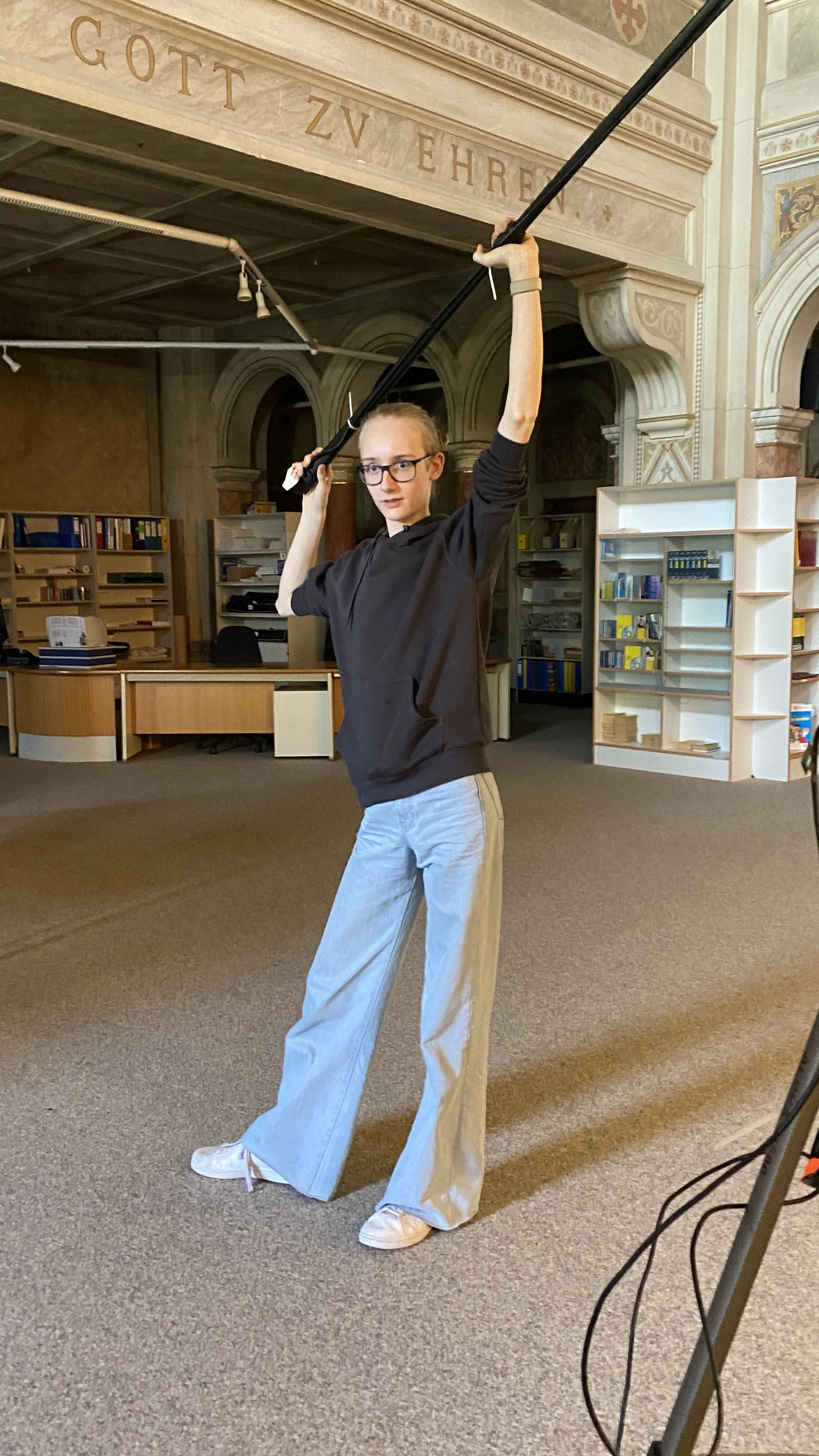 Junge mit Brille holt ein Schwert über dem Kopf in einem Raum mit Bücherregalen.