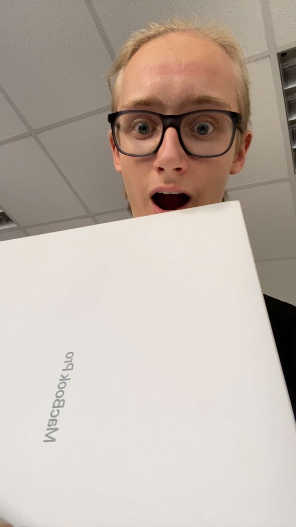 Ein junger Mann mit Brille hält ein Buch mit der Aufschrift "WISCBOK bsl" und sieht überrascht aus.