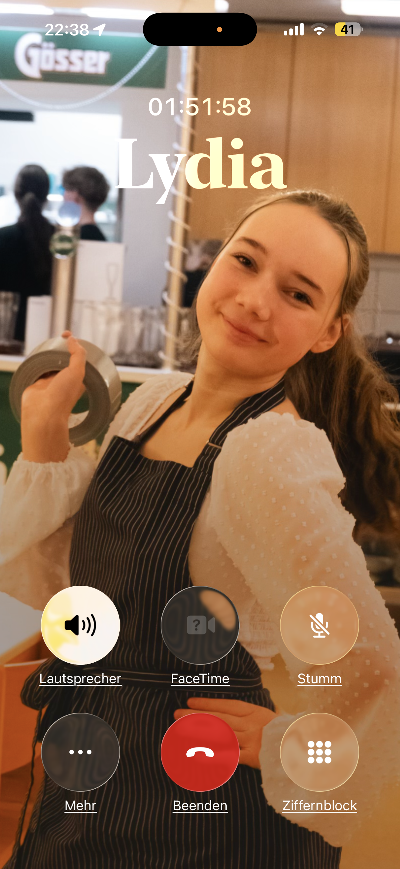 Junge Frau in einem Restaurant, trägt eine schwarze Schürze und hält waschband in der Hand, im Hintergrund andere Menschen, Restaurant-Umgebung.