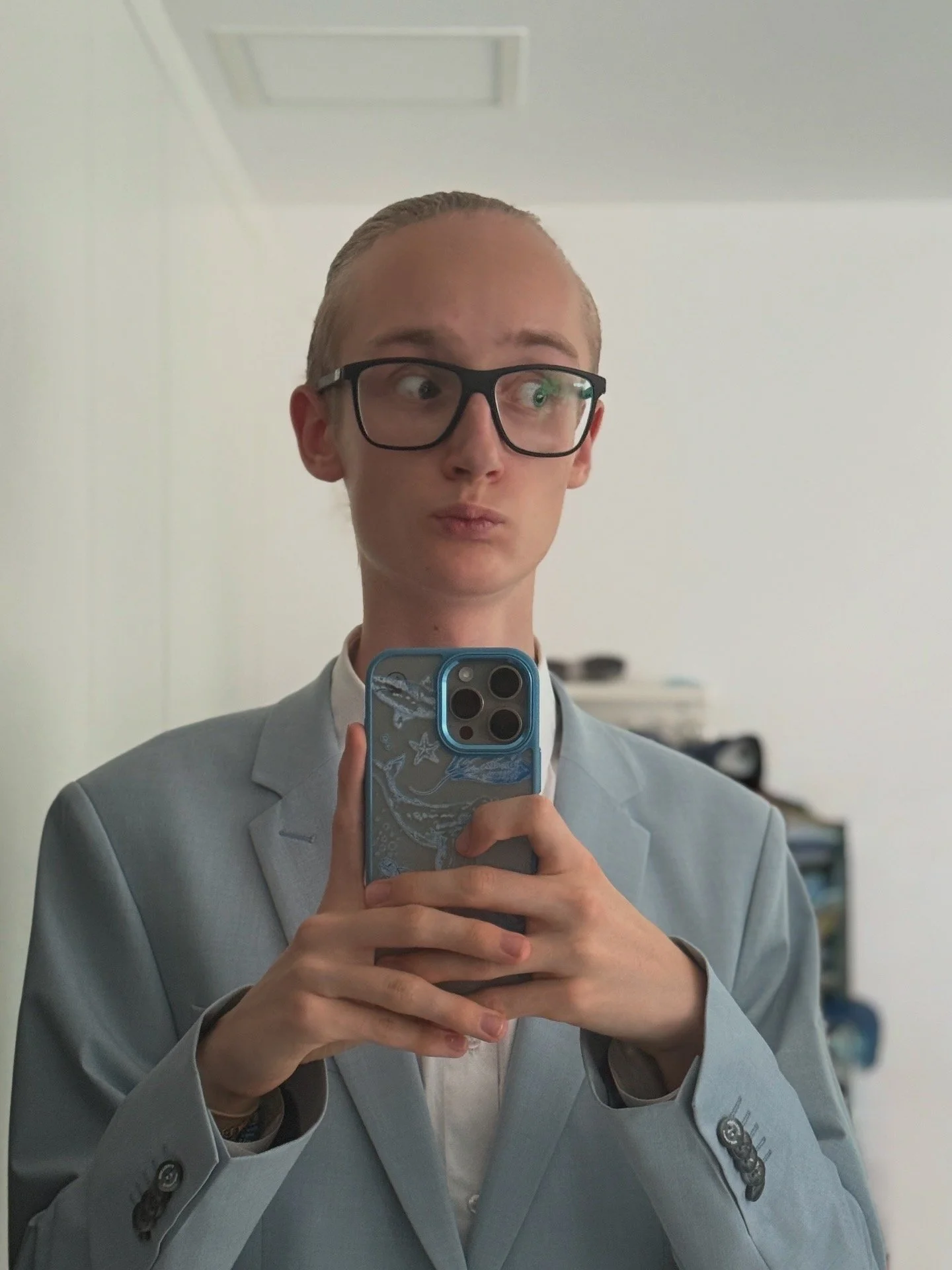 Junge Person in Brille und Anzug macht Selbstporträt mit Smartphone vor einem Spiegel.