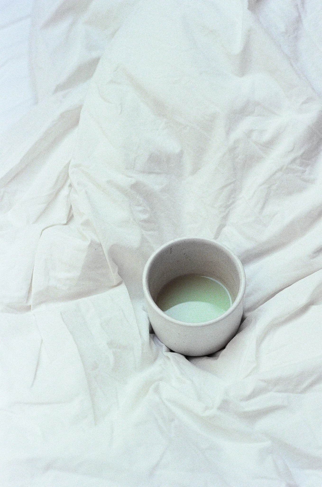 A small white cup filled with a pale green liquid placed on crumpled white tissue paper.