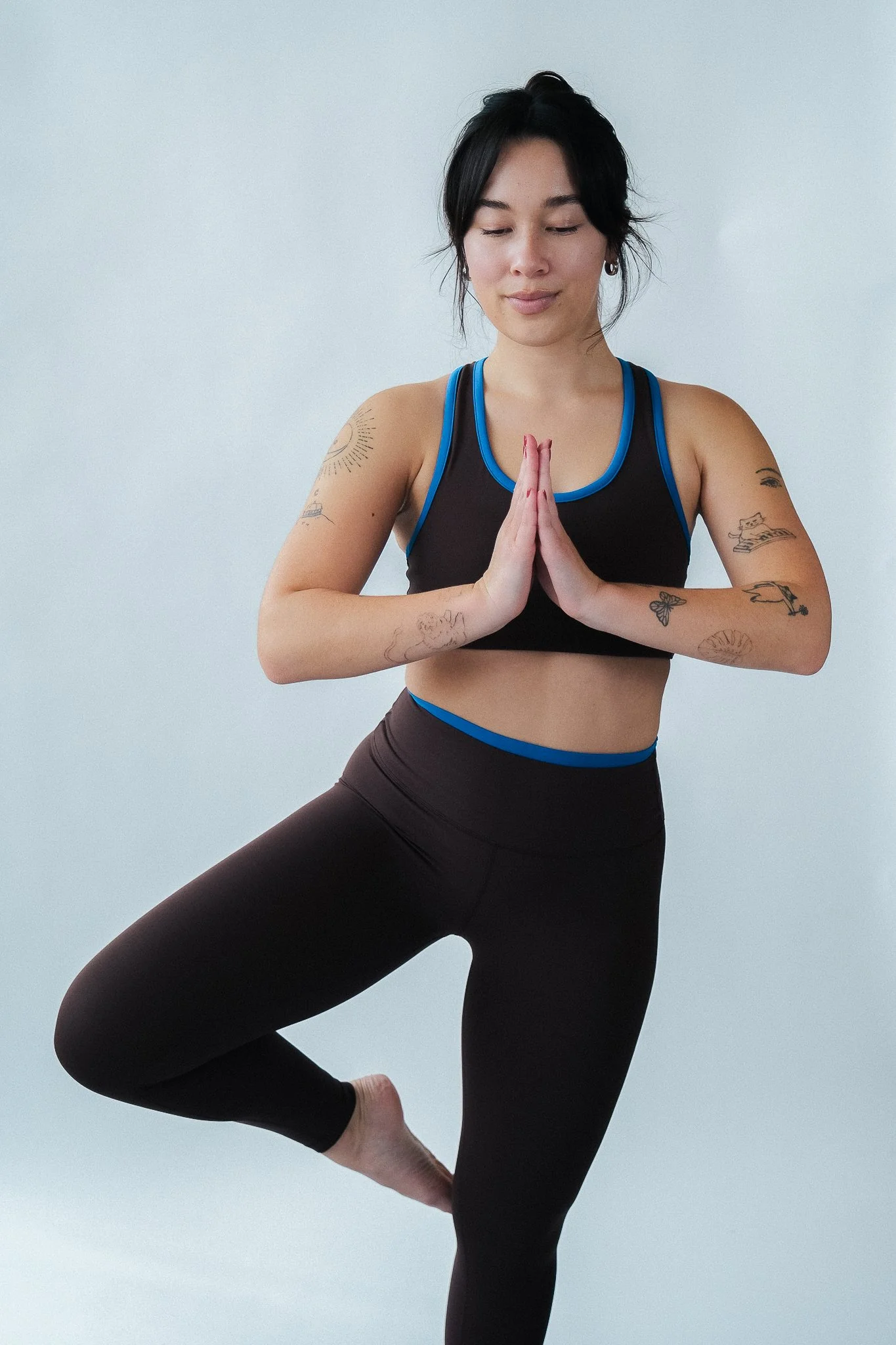 A woman in athletic attire practicing yoga in a tree pose with hands in prayer position and one foot resting on her inner thigh.