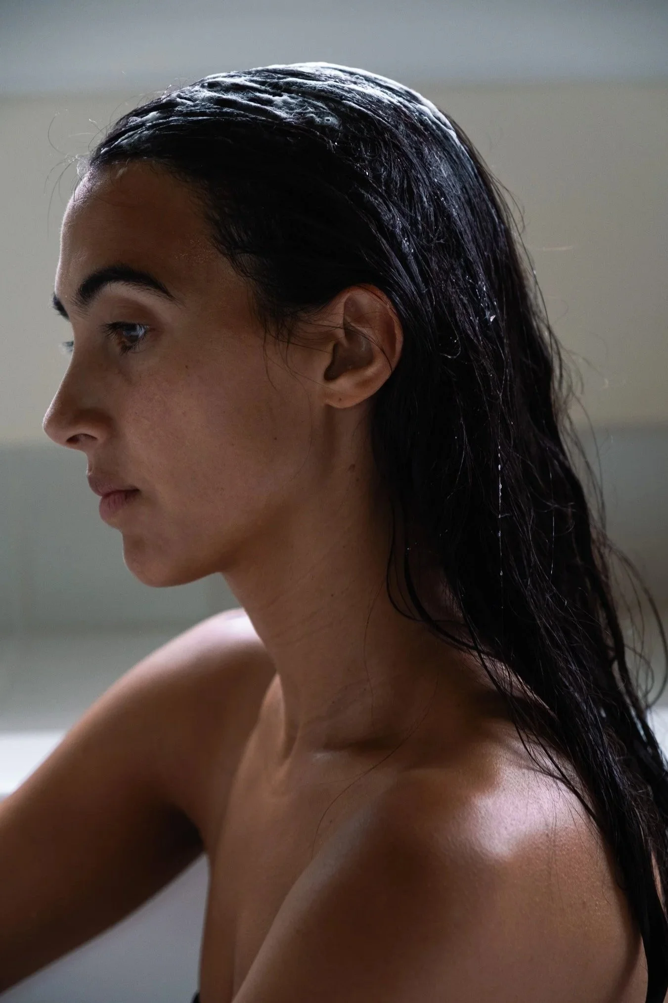 A woman with wet, dark hair sitting in profile, with natural lighting highlighting her face and shoulders.