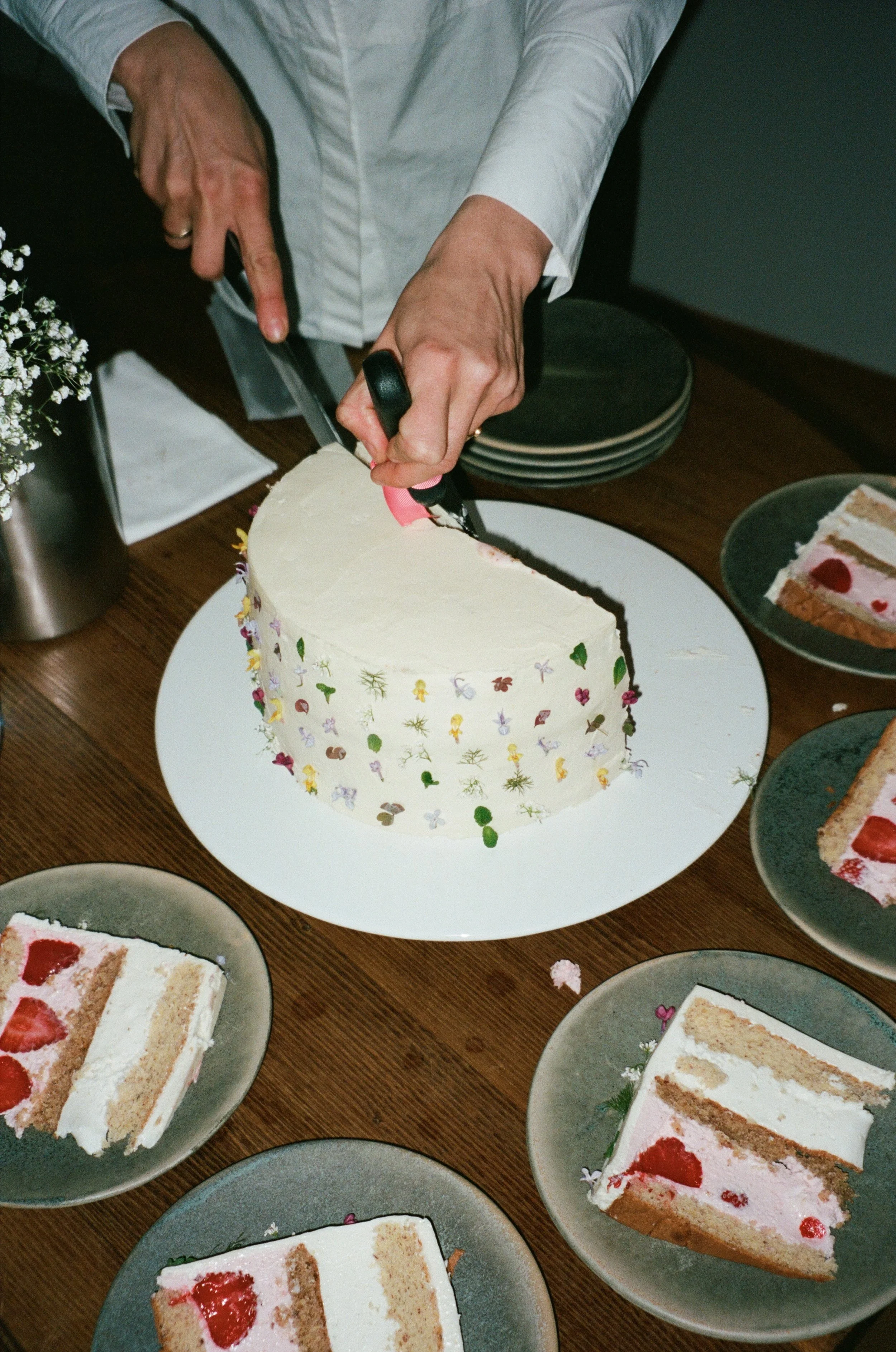 Person cutting a slice of white cake with colorful sprinkles, surrounded by similar slices on plates captured by a wedding photographer in Zürich Switzerland