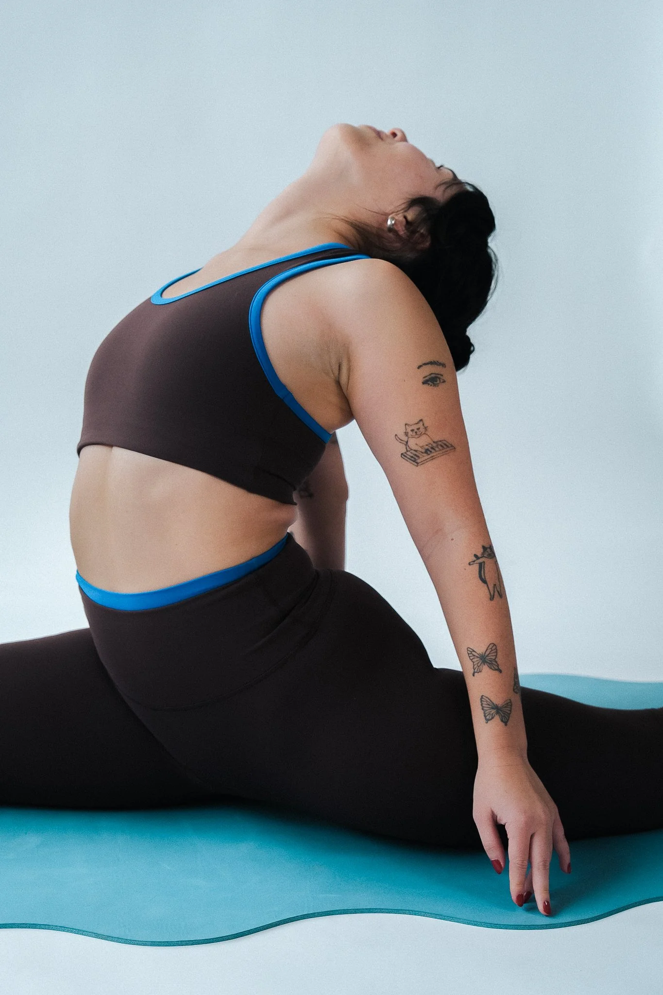 A woman practicing yoga, stretching on a yoga mat with a light blue background.