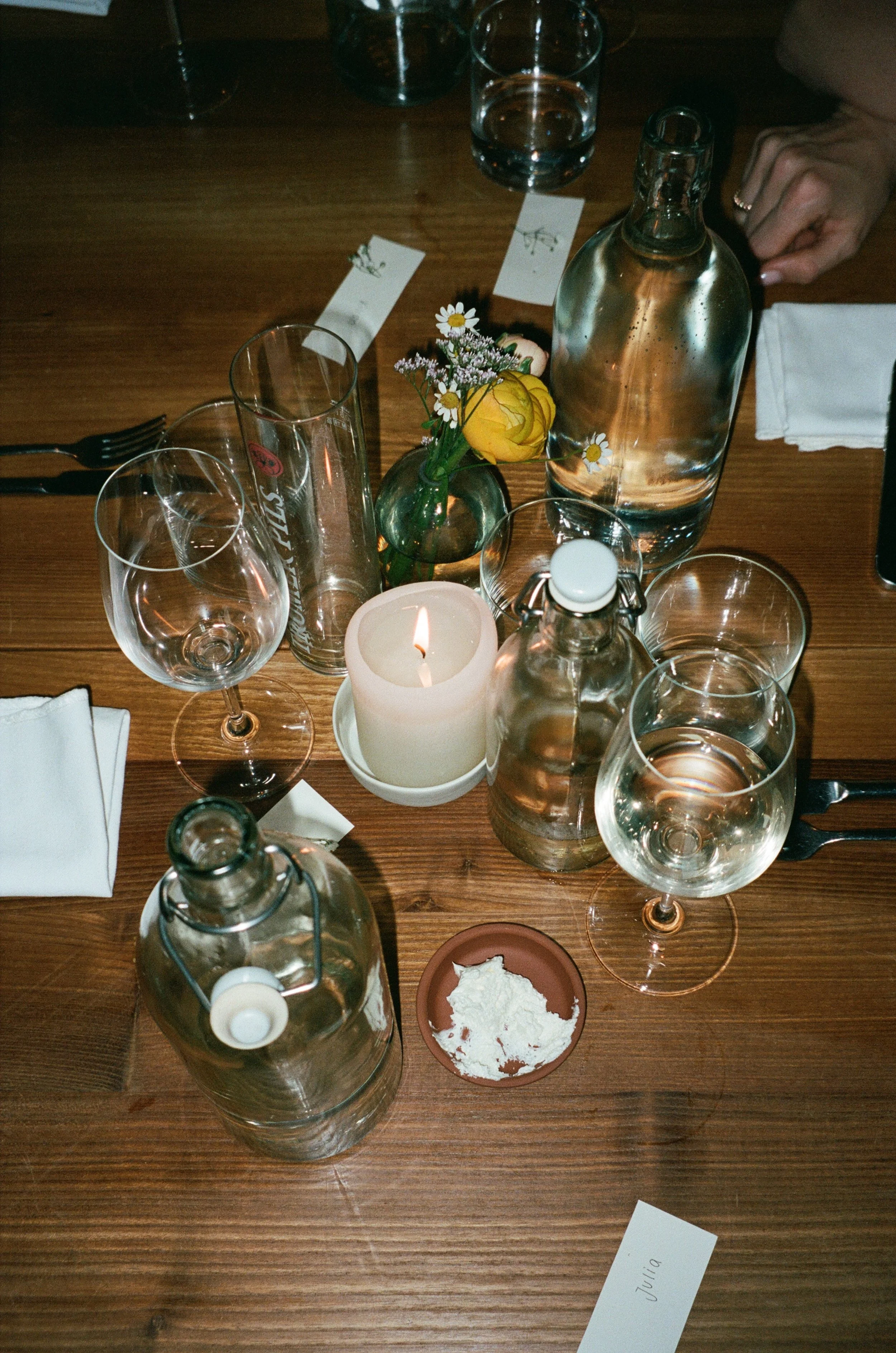 A table setting at a restaurant with glassware, water bottles, a candle, a small flower arrangement, white napkins, and place cards.