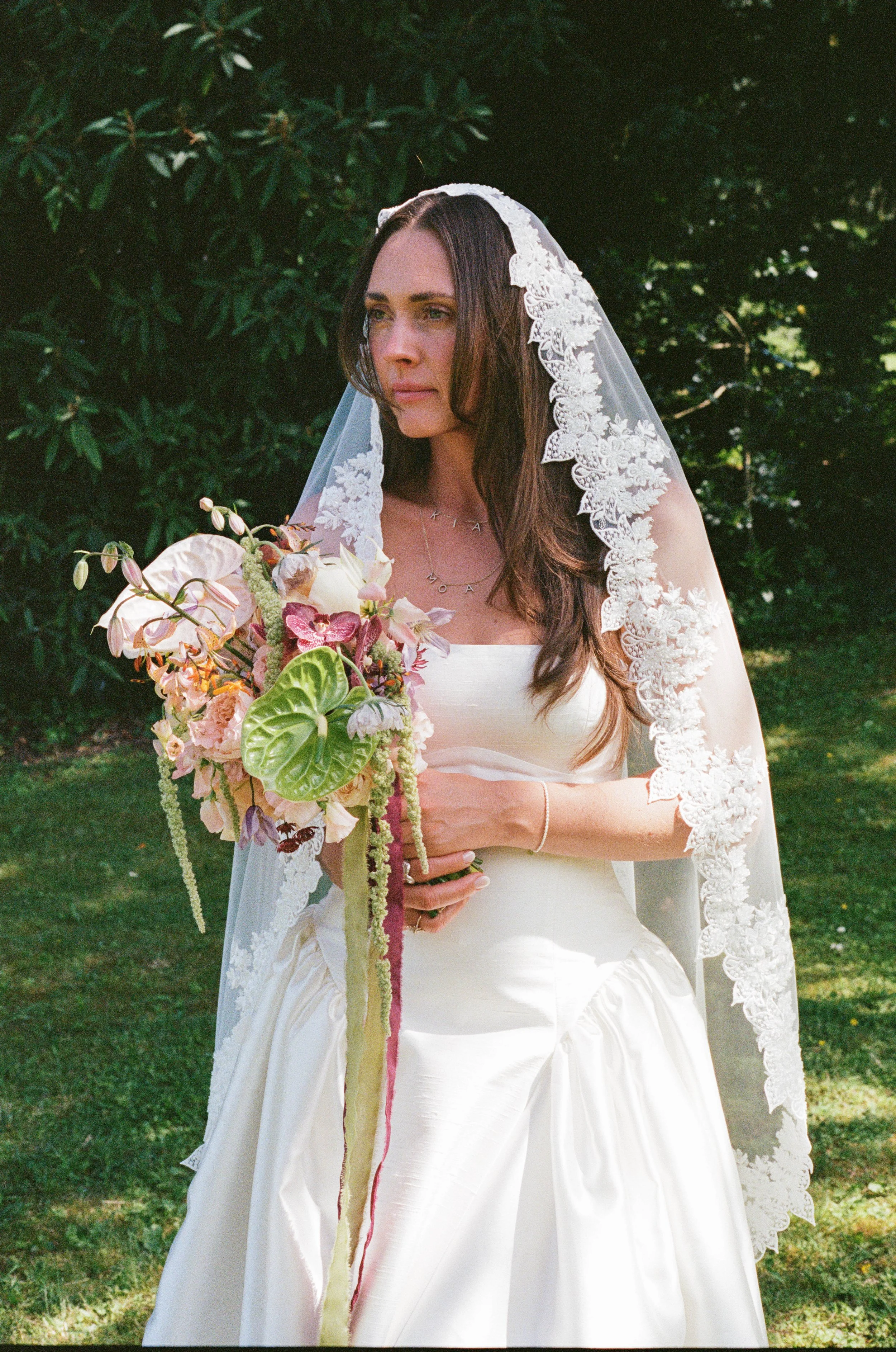 A modern styled bride with long brown hair, wearing a white wedding dress and lace veil, holding a bouquet of flowers with pink, white, and green elements in Zurich Switzerland.