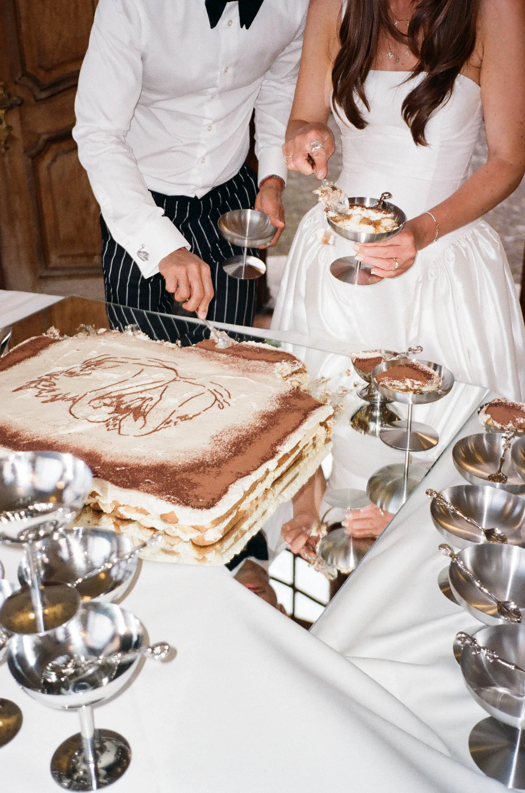 A modern stylish wedding cake with a sketch of a bride on top and a couple cutting the cake, with the bride wearing a white gown and the groom in a white shirt with black tie and striped pants in Switzerland.