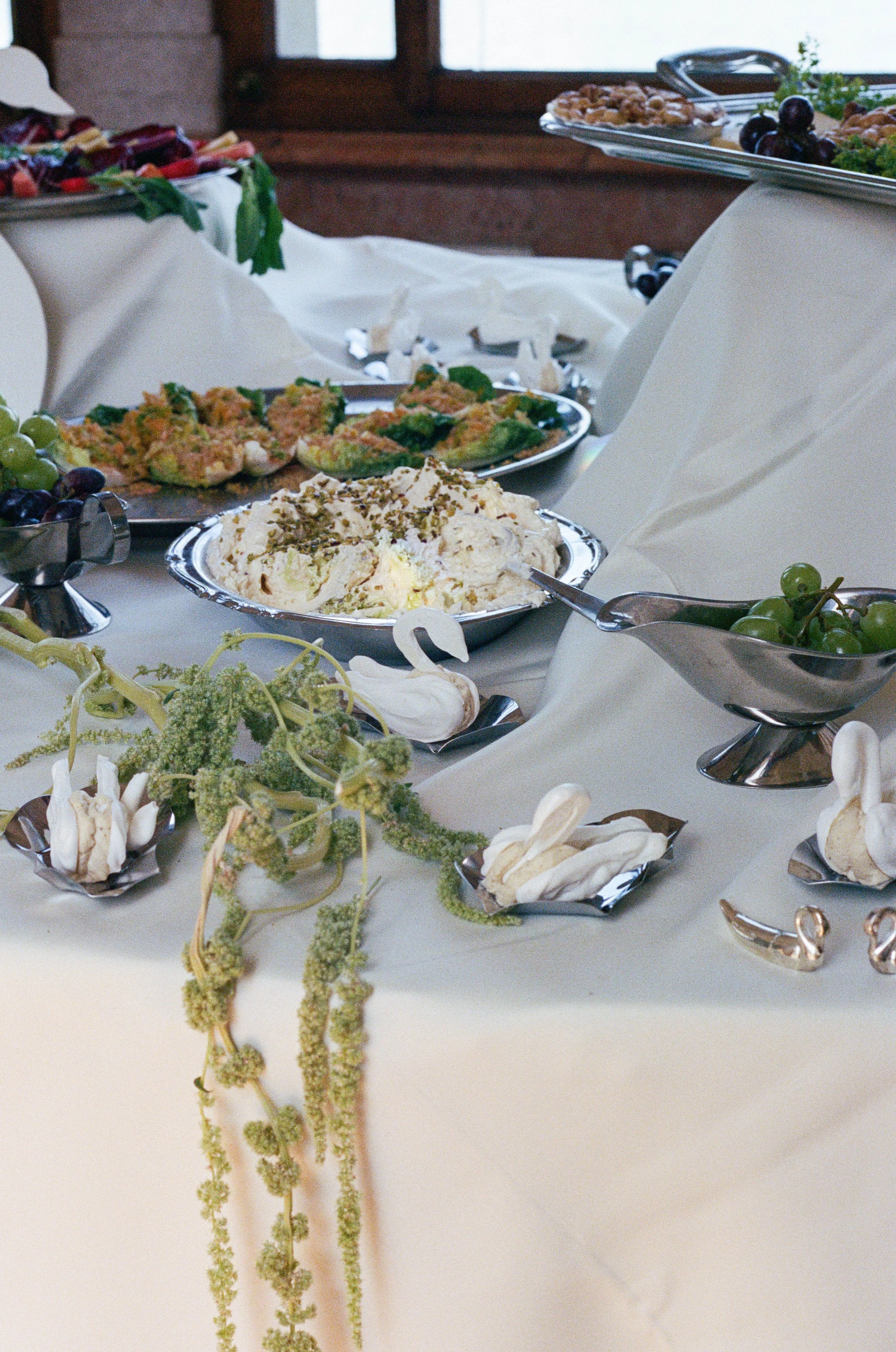 A modern styled wedding table able with appetizers, garnished with grapes and herbs, covered with a white tablecloth, in a room with wooden window frames captured by a wedding photographer in Zürich Schweiz. 