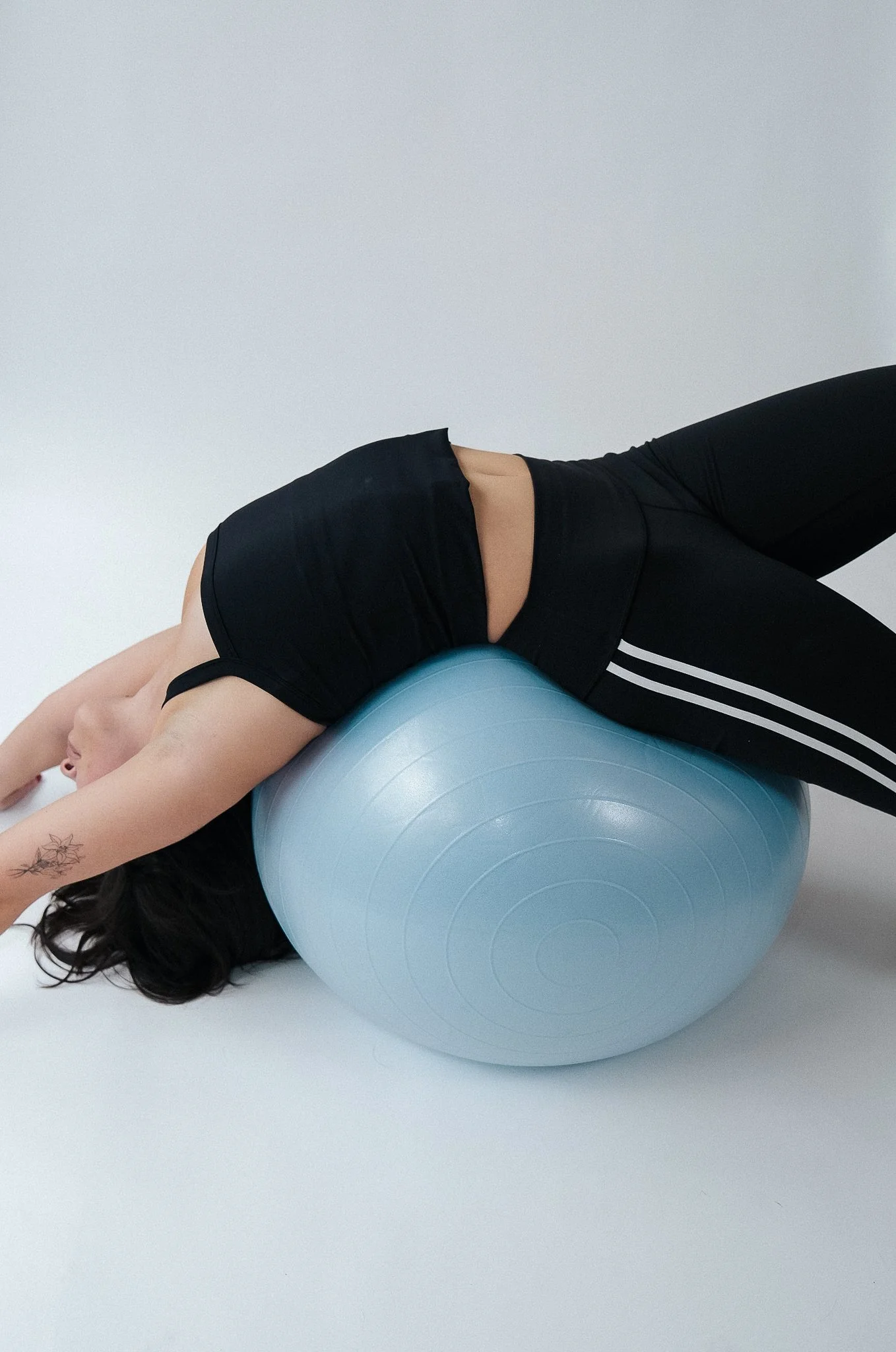 Woman lying on her stomach on a blue exercise ball, in a fitness setting.