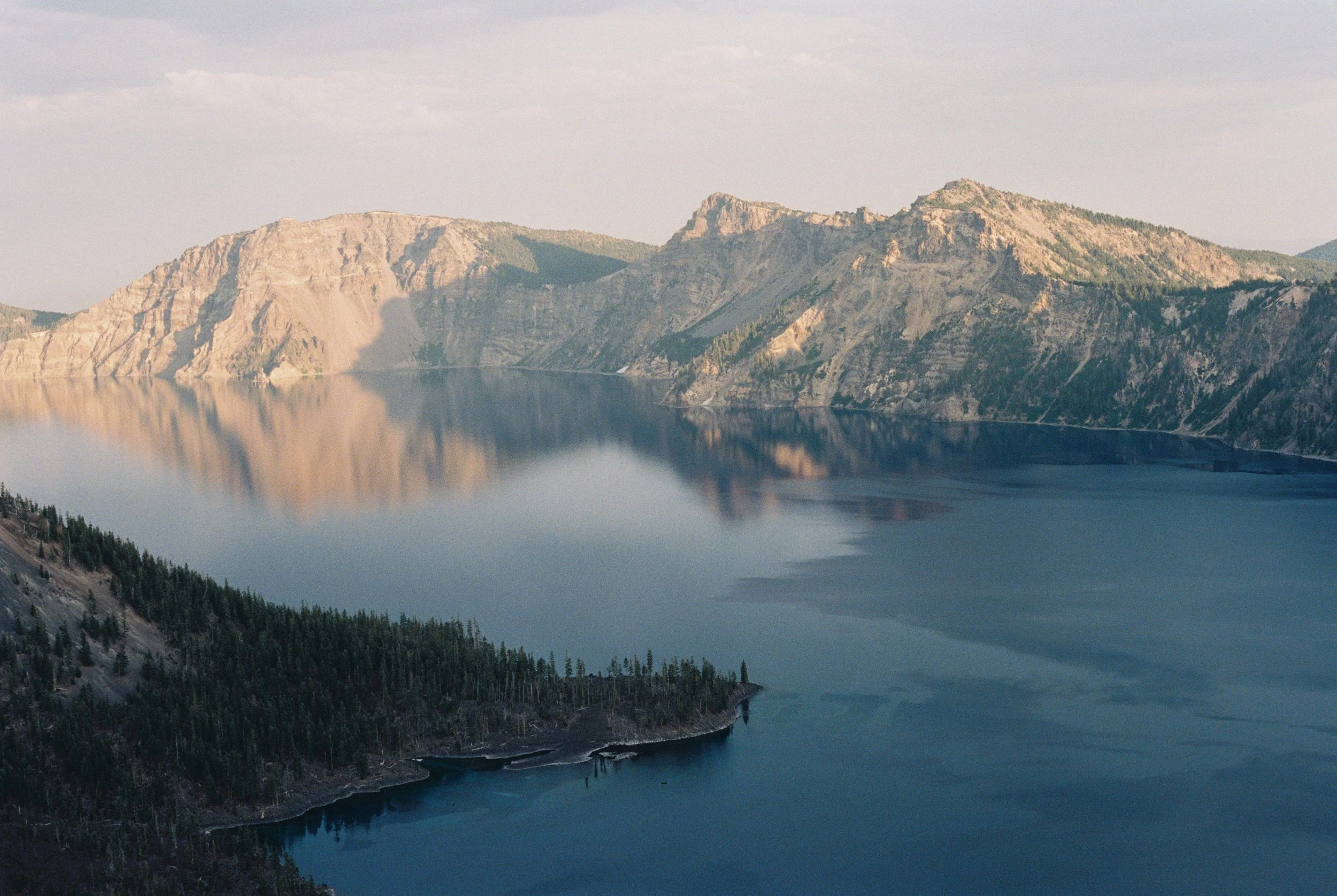 A large body of calm water reflecting mountains and a cloudy sky.