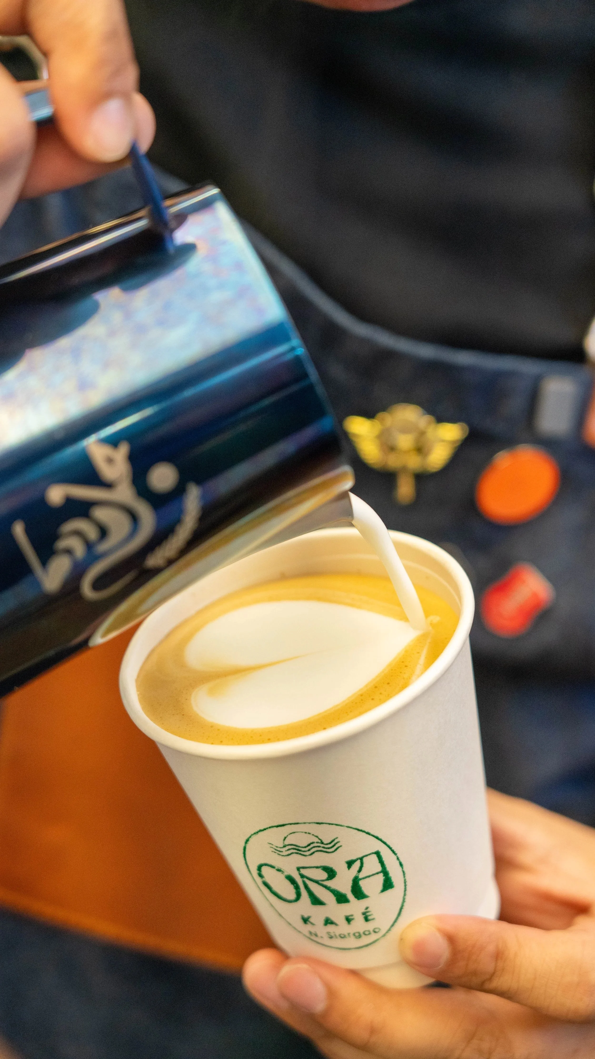 Person pouring creamer into a cup of coffee at Ora Kafé.