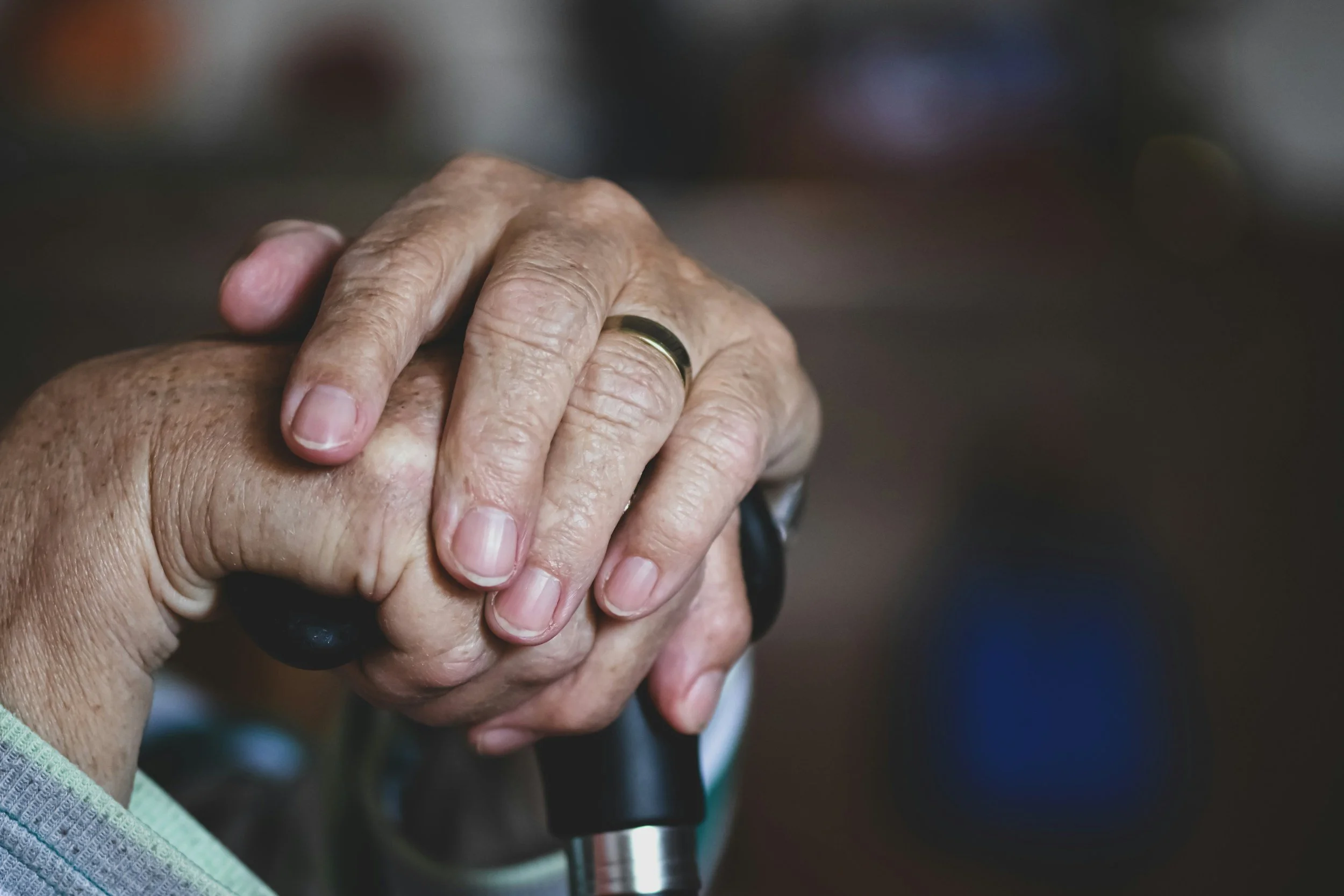 Close-up of elderly person's hand with a wedding ring, gripping a cane handle.