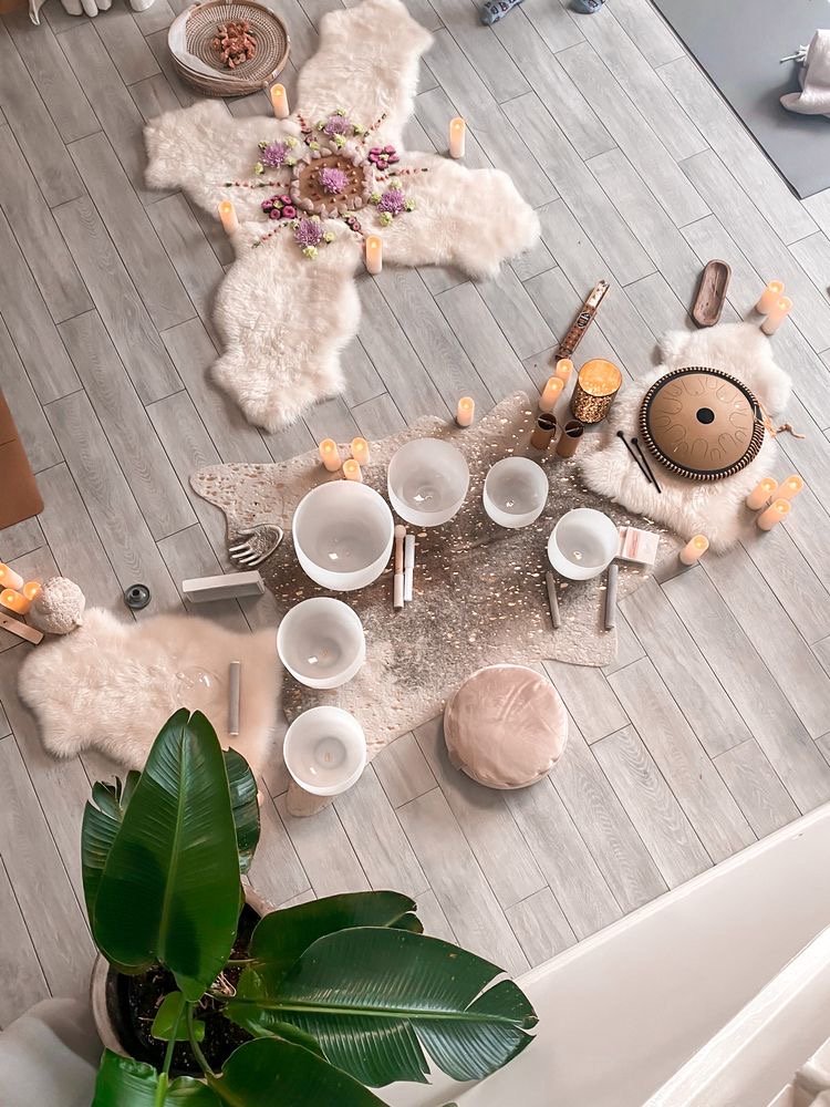 Bohemian-style indoor decorative setup with candles, plush rugs, flowers, a round drum, and a large green plant near the bottom left corner.