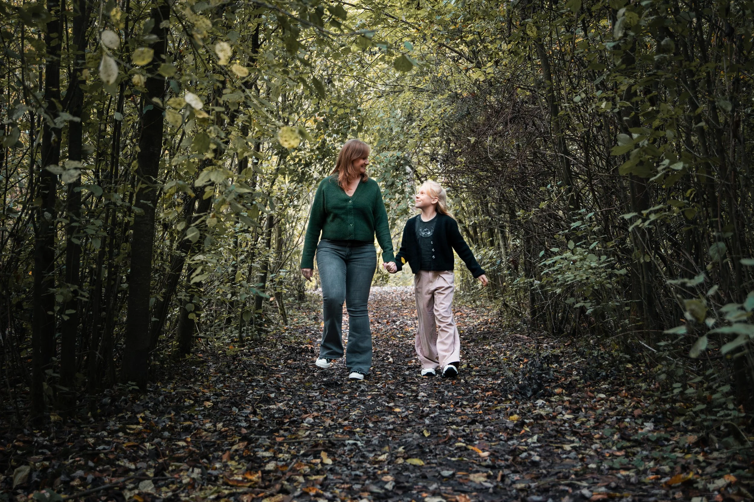 Intieme connectie: Moeder en dochter lopen hand in hand en kijken elkaar liefdevol aan tijdens een spontane fotoshoot in een herfstbos bij Leidschendam - Zoetermeer